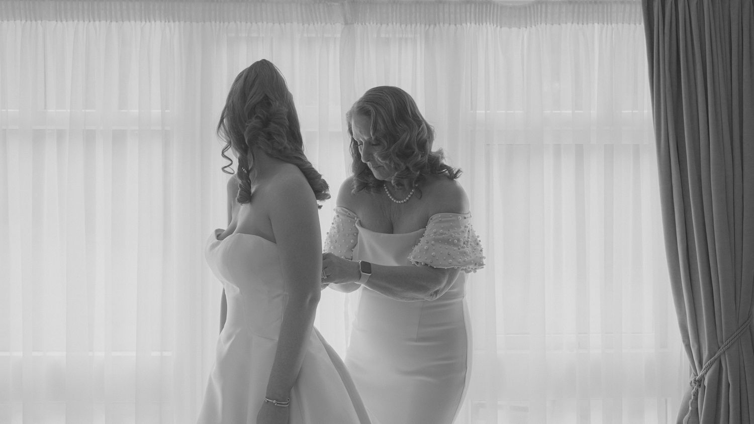 Black and white image of bridal preparation with elegant window light.