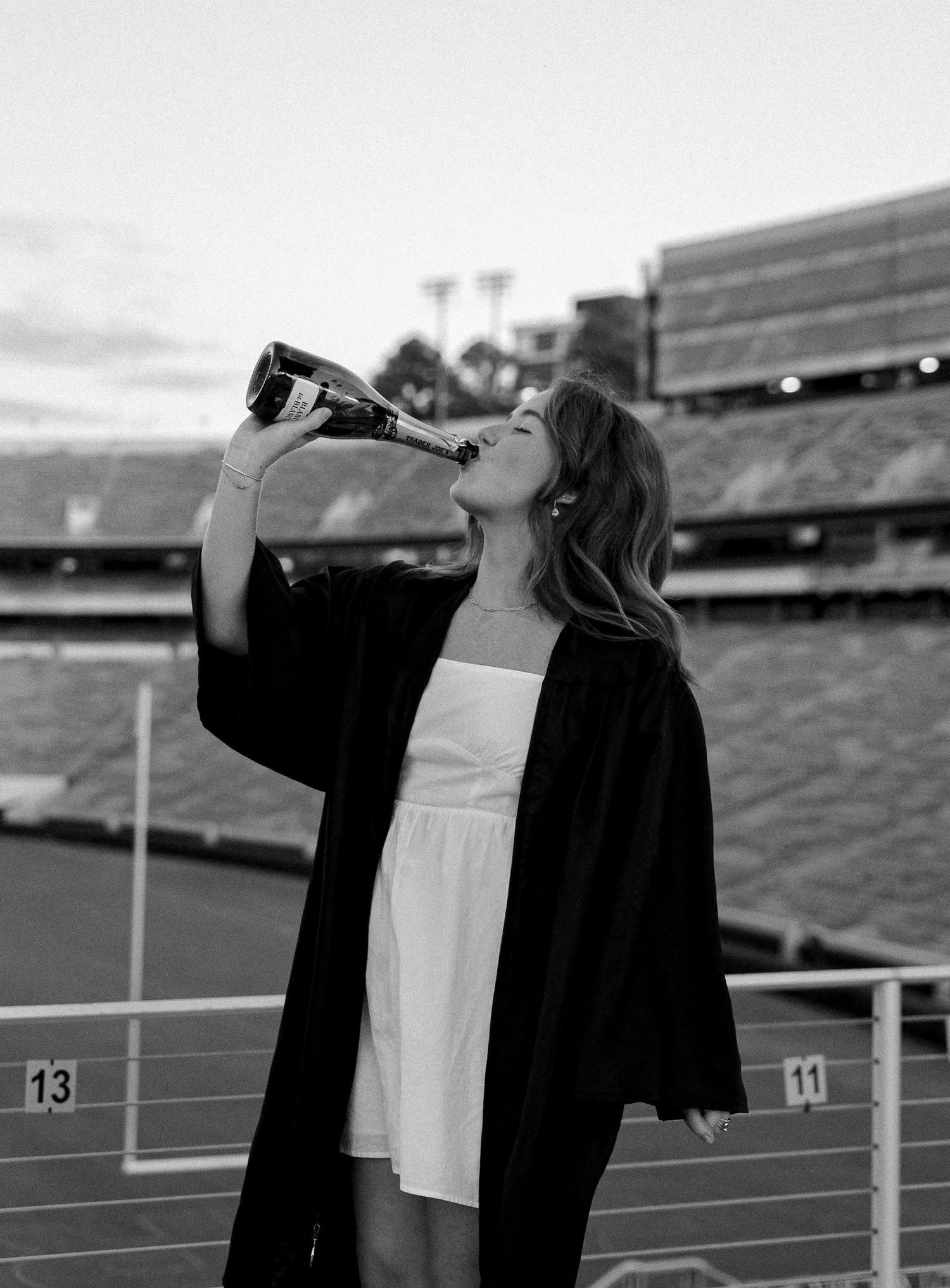 Person in black jacket drinking from bottle at stadium bleachers in monochrome.