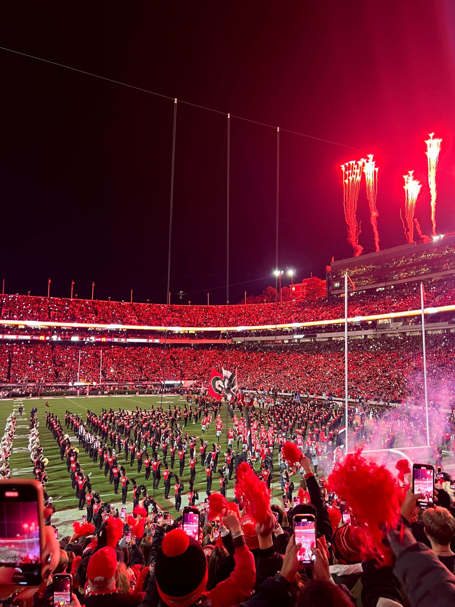 A packed stadium glowing with red lights and fireworks during a nighttime sporting event.