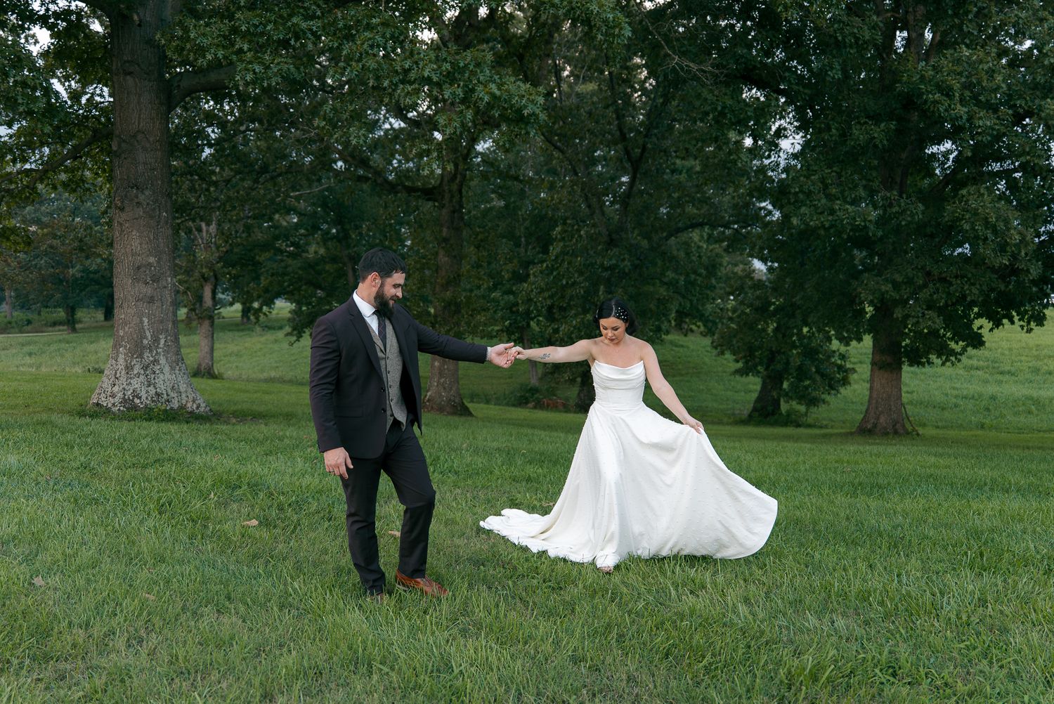 Wedding couple walking and posing together on grassy lawn with trees.