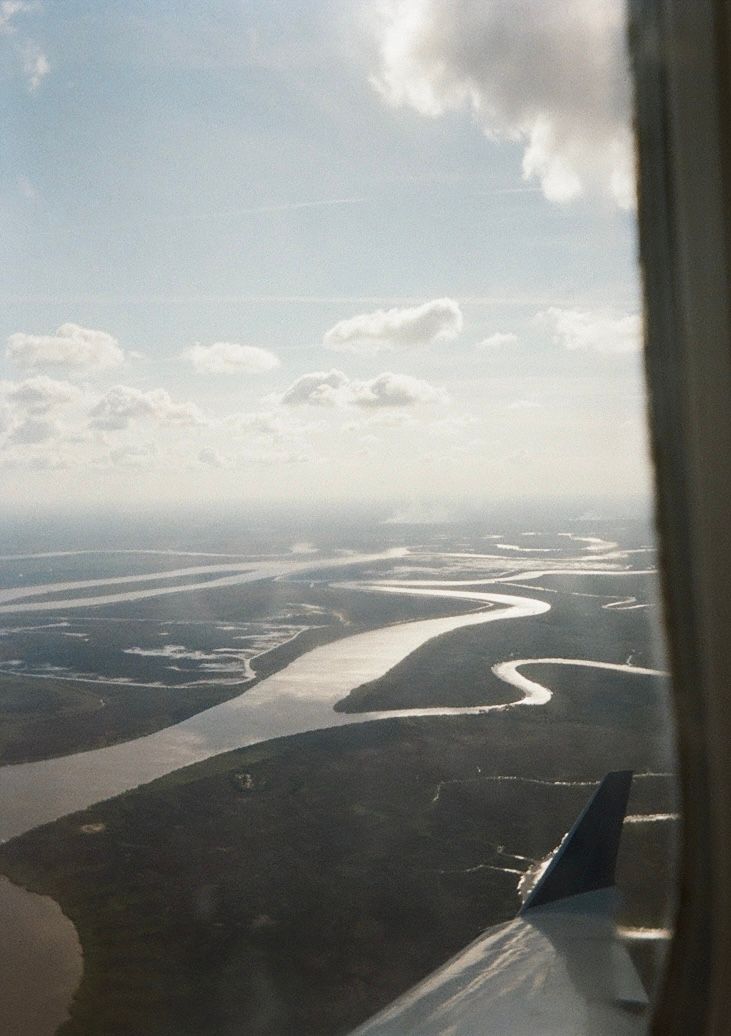 Aerial view of winding rivers and coastline through an airplane window on a cloudy day.