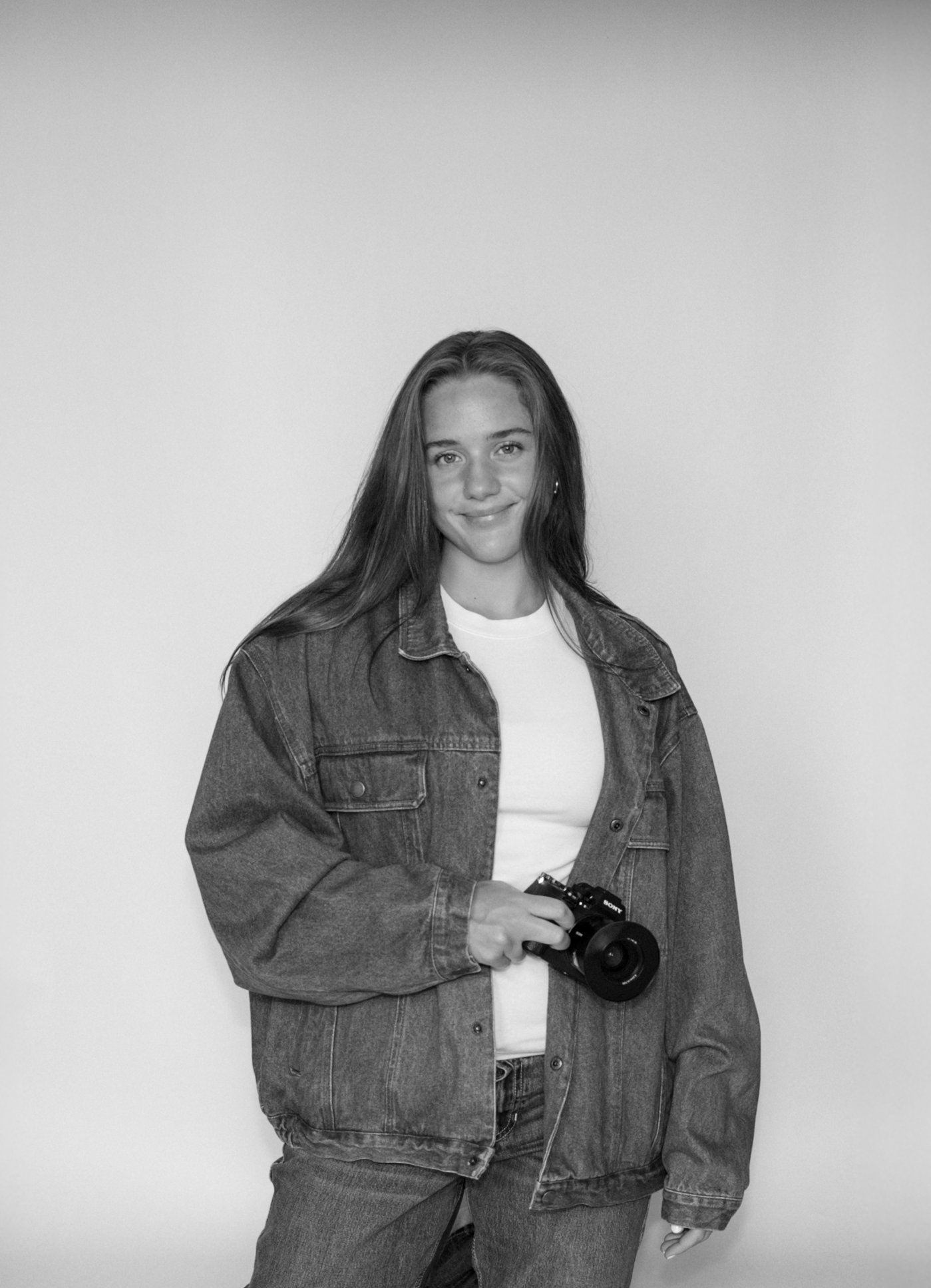 Figure poses in oversized denim jacket and white top against neutral background.