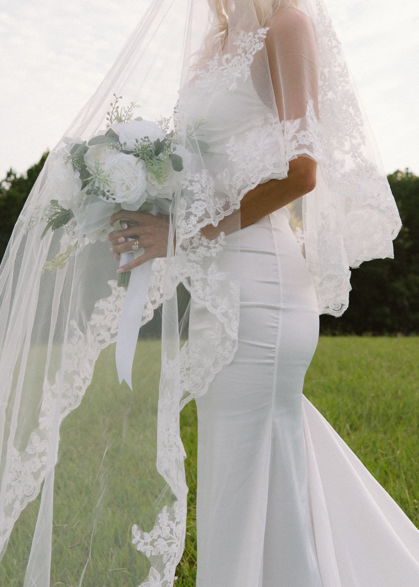 Ethereal wedding dress with lace details photographed against a natural outdoor backdrop.