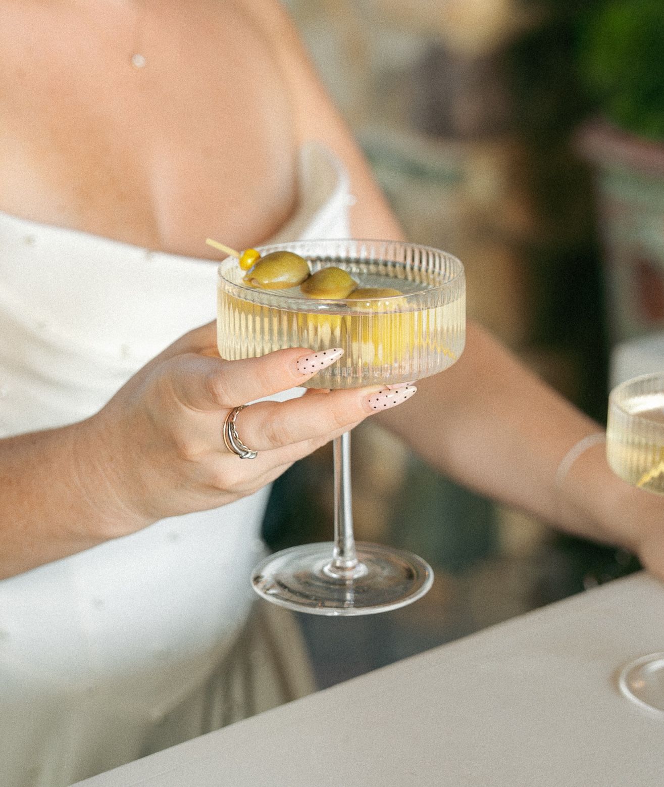 Elegant champagne cocktail in a crystal coupe glass garnished with citrus held by someone in white.