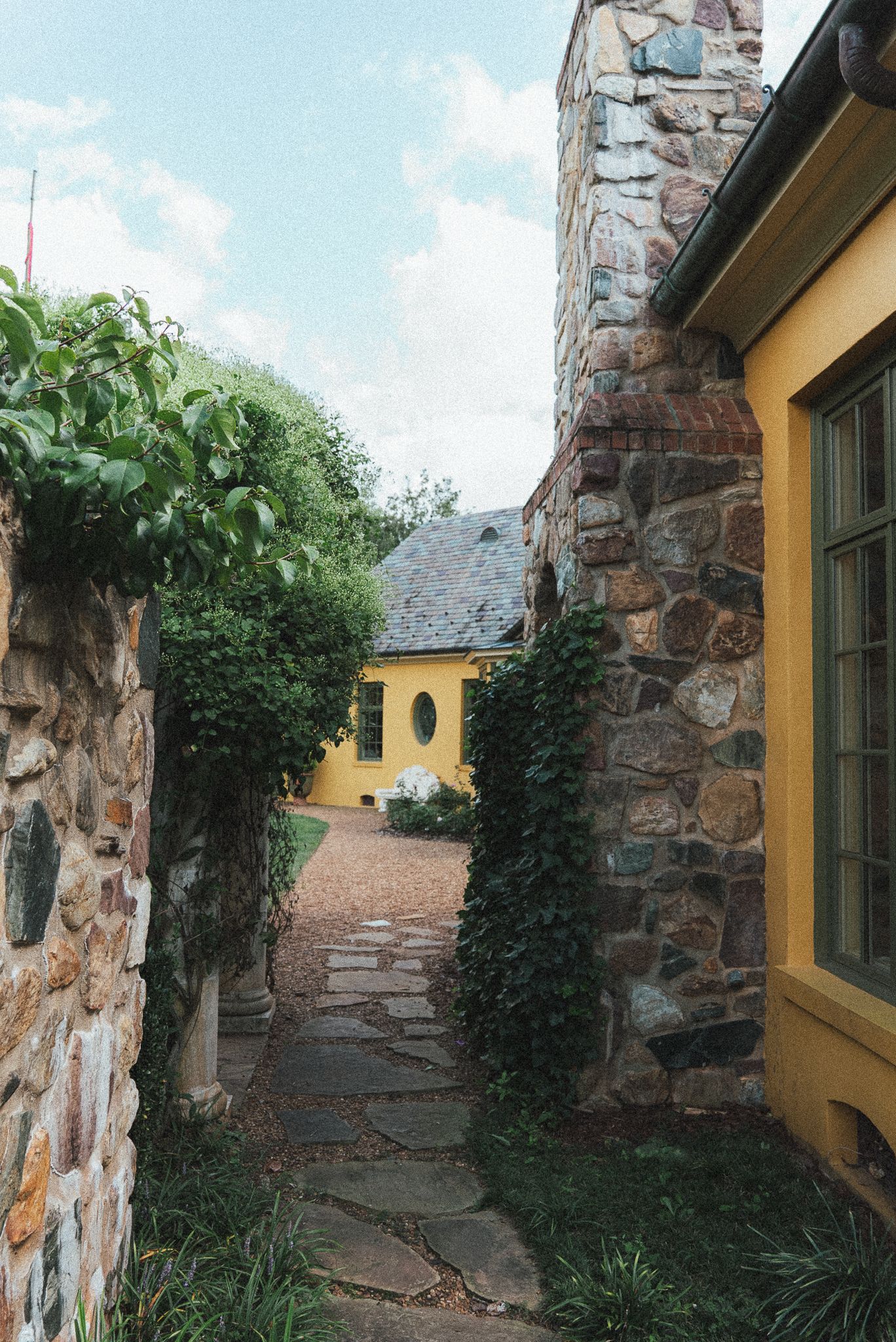 Stone wall exterior of a yellow building with climbing vines and greenery.