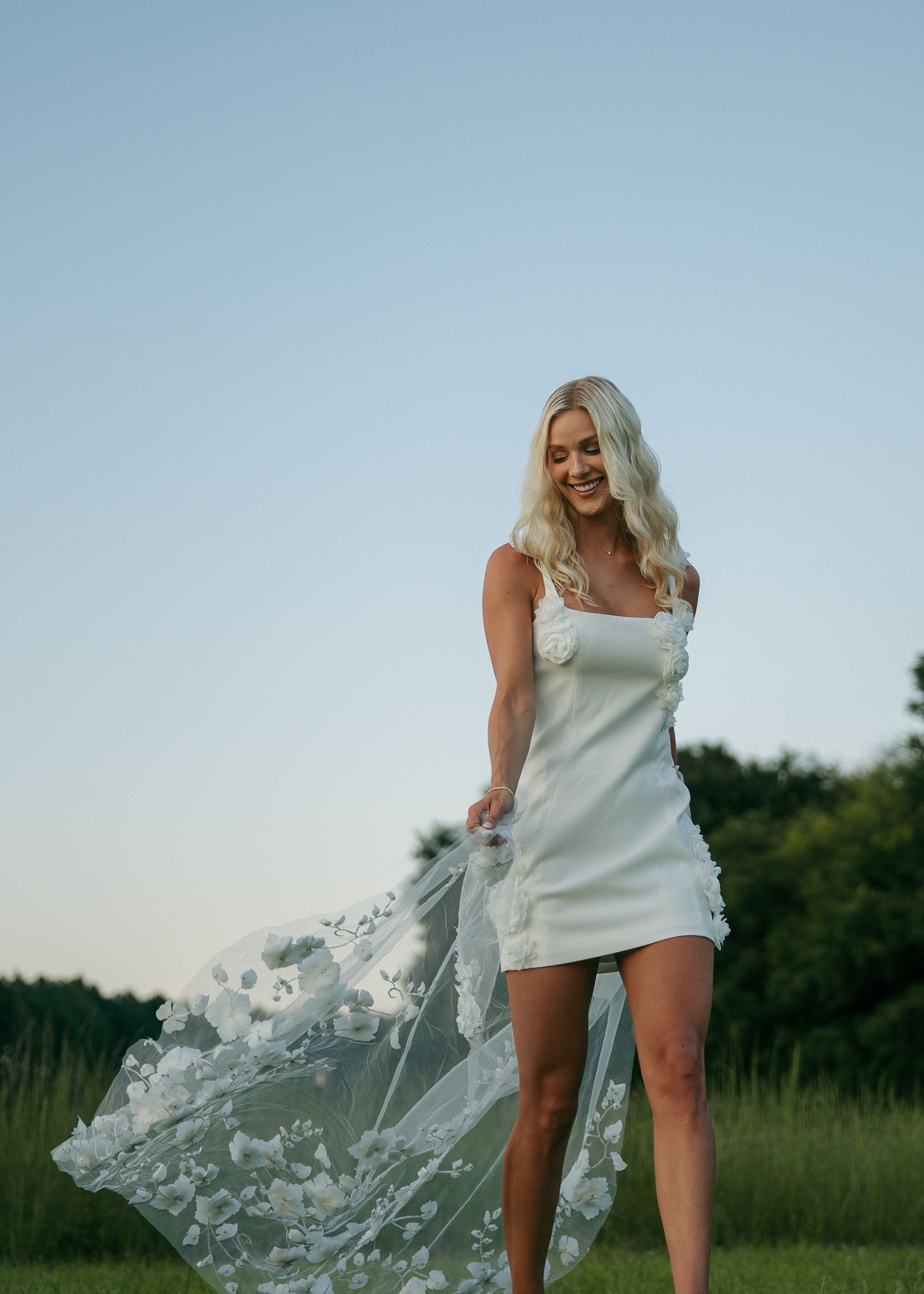 Woman in white mini dress twirling with flowing fabric against blue sky.