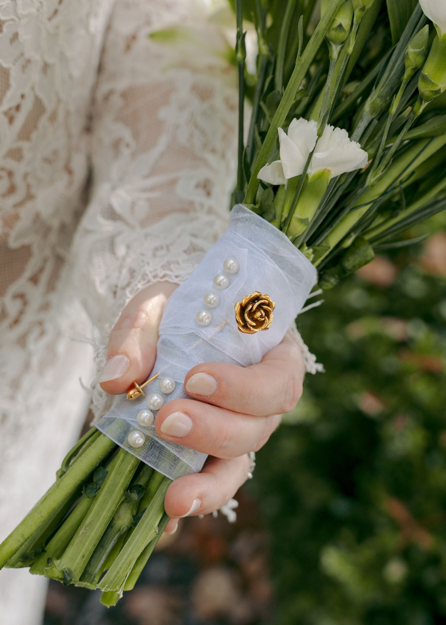 Close-up of hands holding a white floral bouquet with decorative pins.