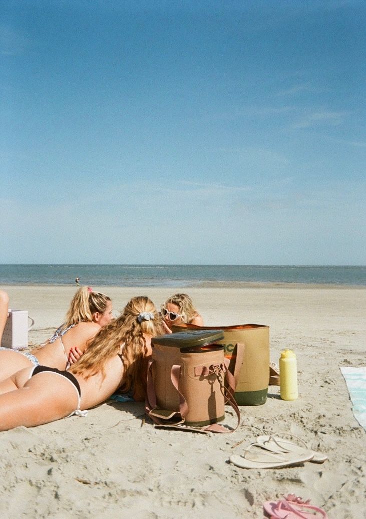 People lounging on a pristine white sand beach with bags and drinks scattered around.