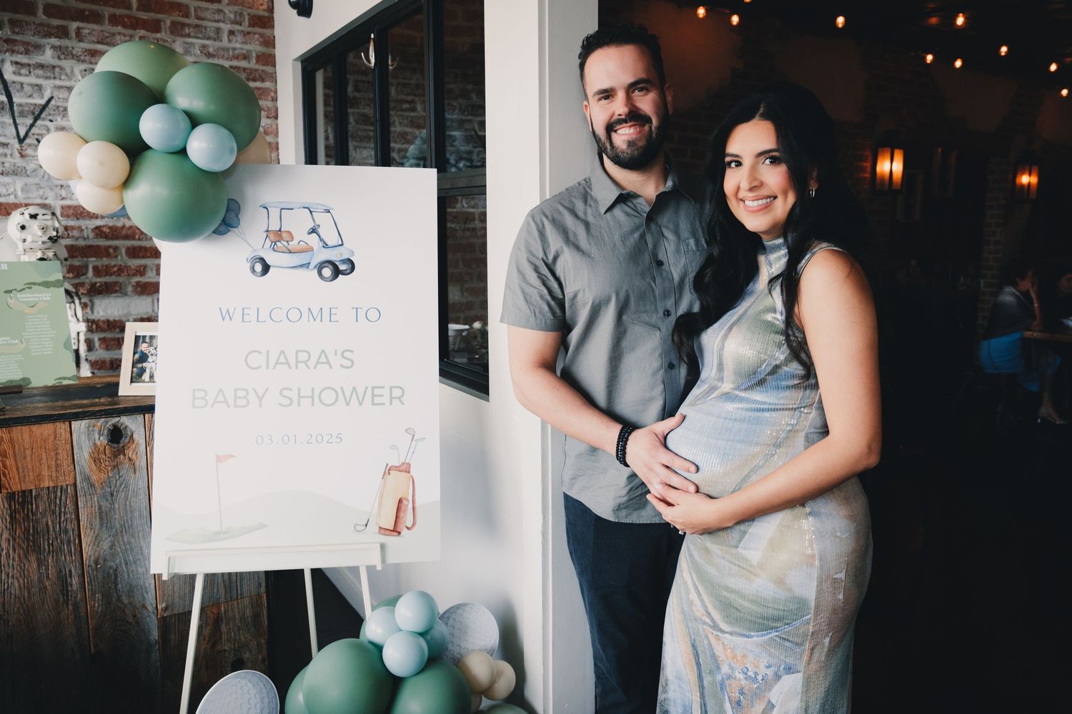 Baby shower celebration with mint green and white balloon decorations against brick wall backdrop.