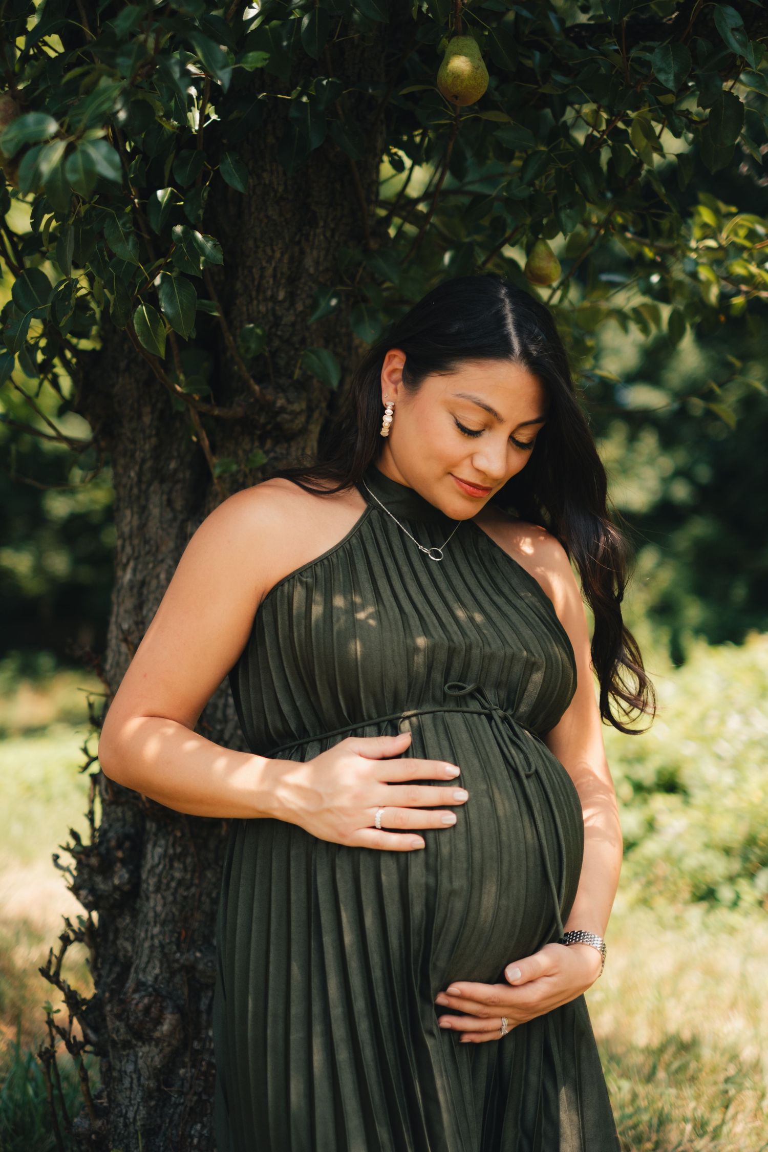 Maternity photos showing a pregnant woman in a dark dress embracing her belly in a garden setting.