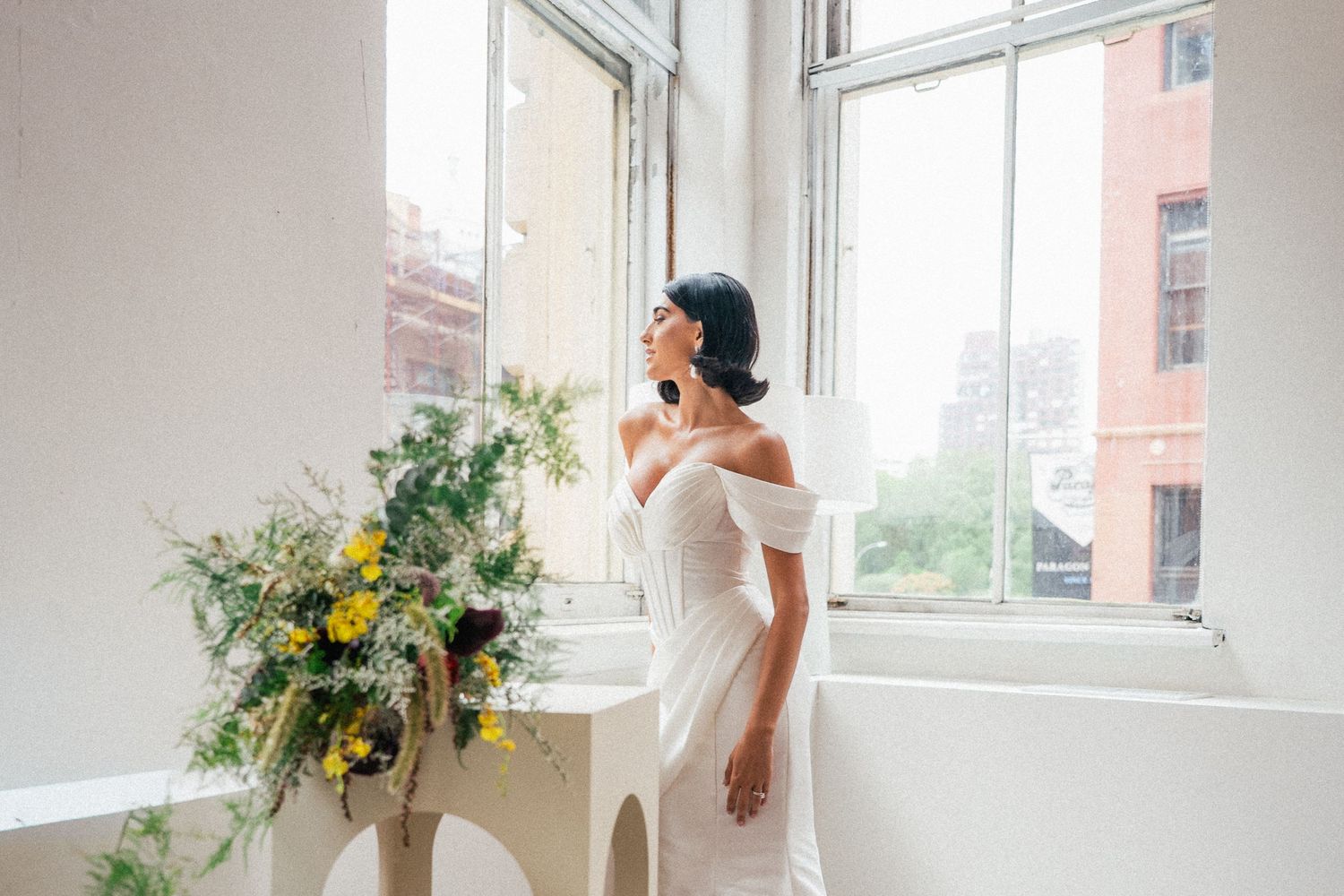 Minimalist bridal photoshoot in bright white room with large windows and floral arrangements.
