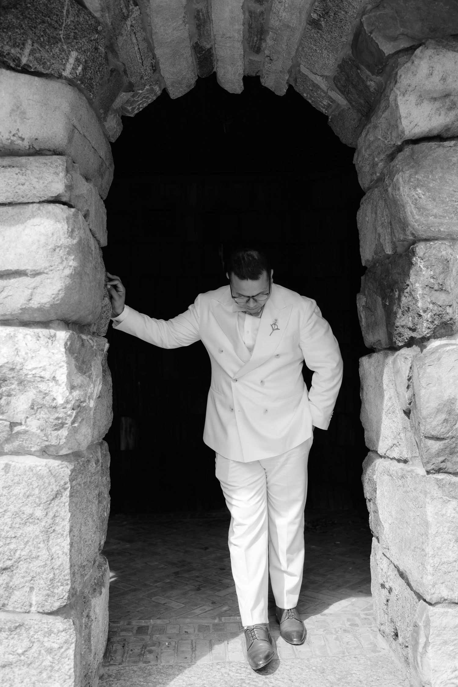 Man in white suit standing in stone archway, black and white portrait photography.