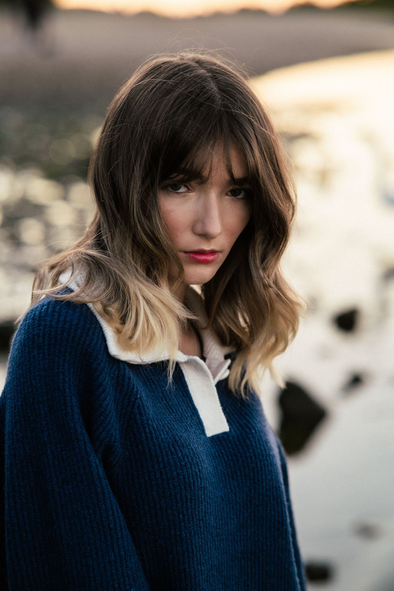 Fashion portrait showing a navy blue sweater and white collar against a sunset backdrop.