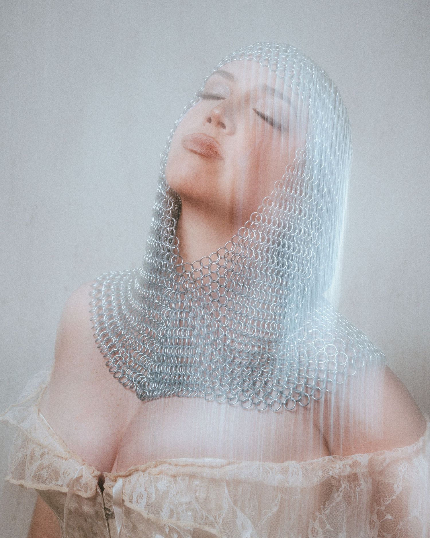 Woman wearing silver chainmail veil with eyes closed in artistic fashion portrait.