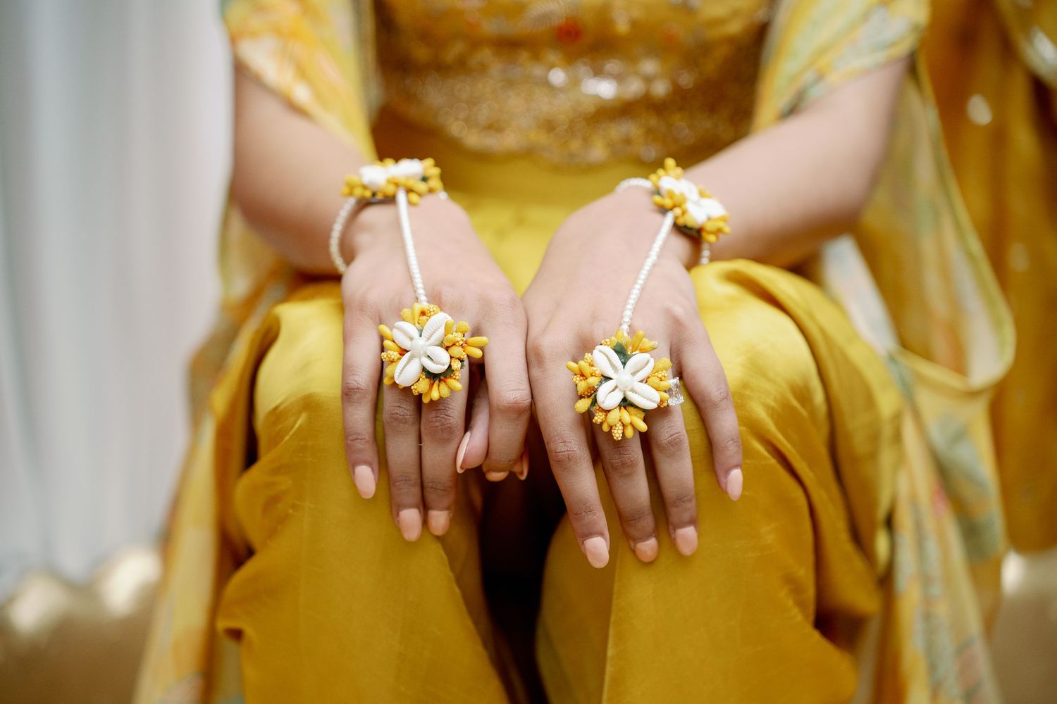 Woman in yellow outfit wearing floral yellow and white jewelry rings and bracelets on both hands.