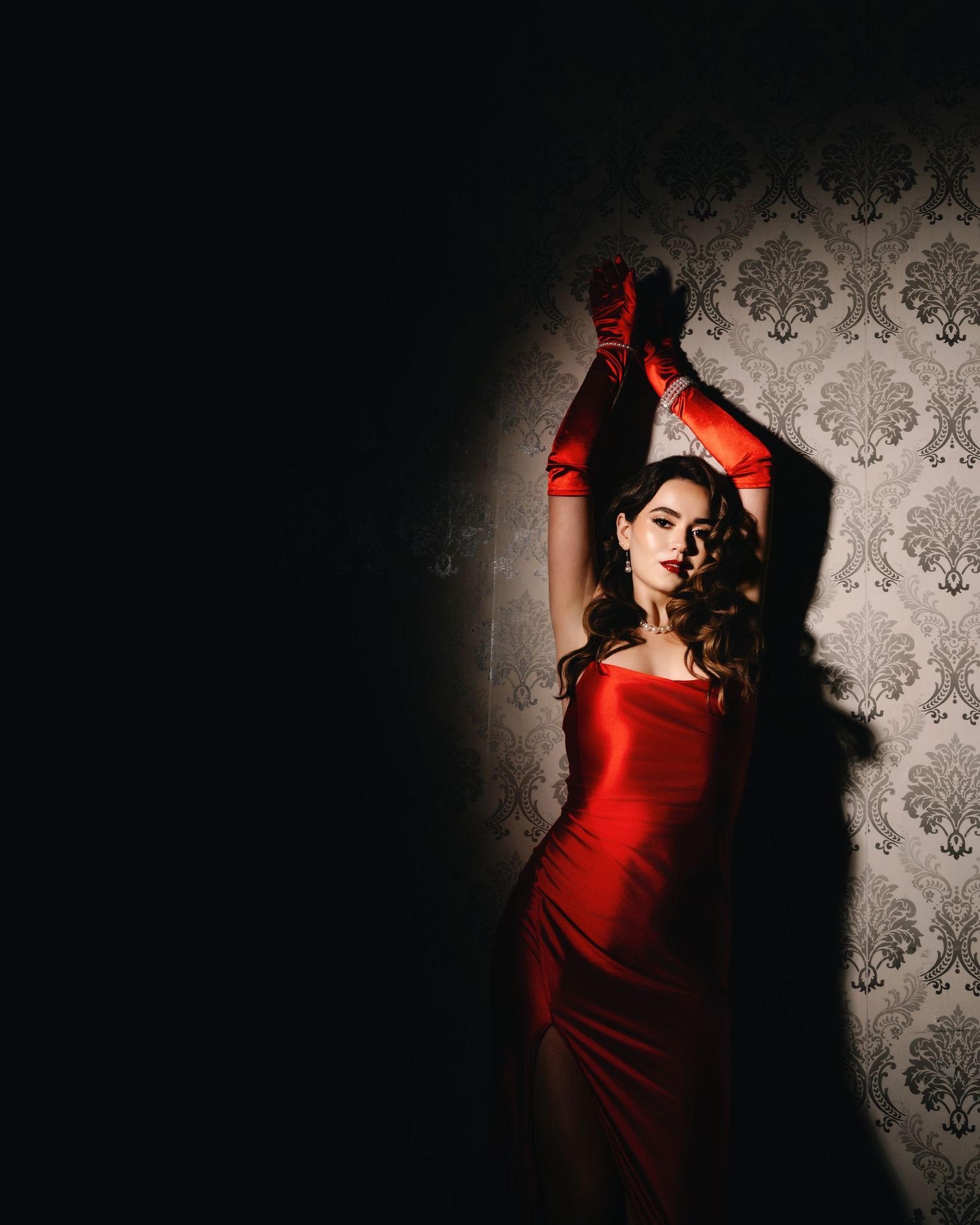 Dramatic portrait series in red dress against patterned wallpaper with moody lighting and shadows creating artistic contrast.