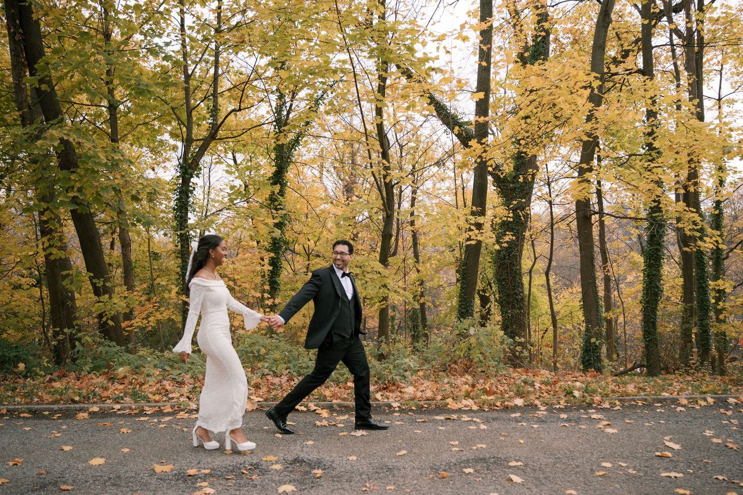 Couple walking together through autumn woods with golden leaves falling on a scenic path.