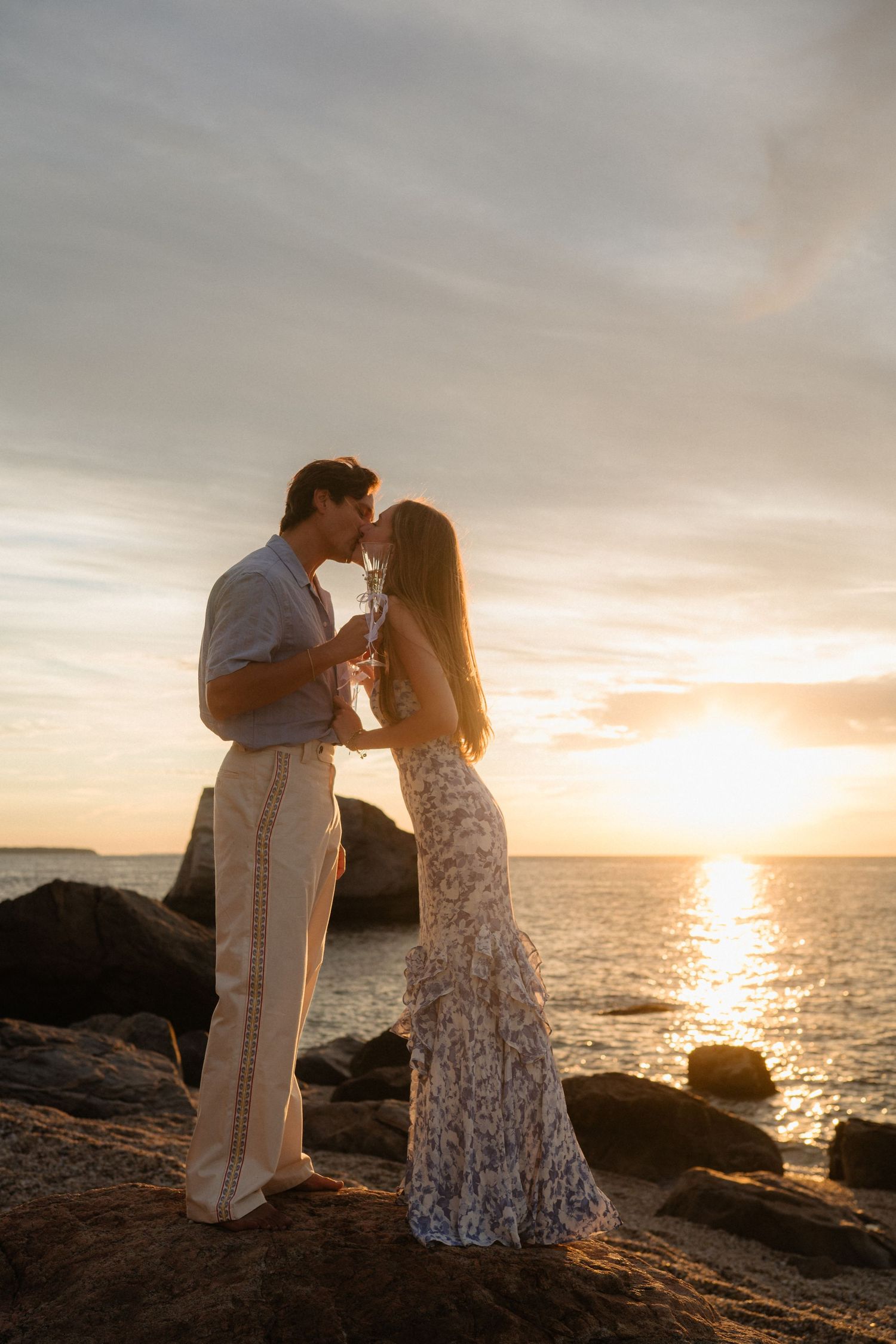 A romantic couple embraces on rocky cliffs overlooking the ocean at sunset in Hawaii.