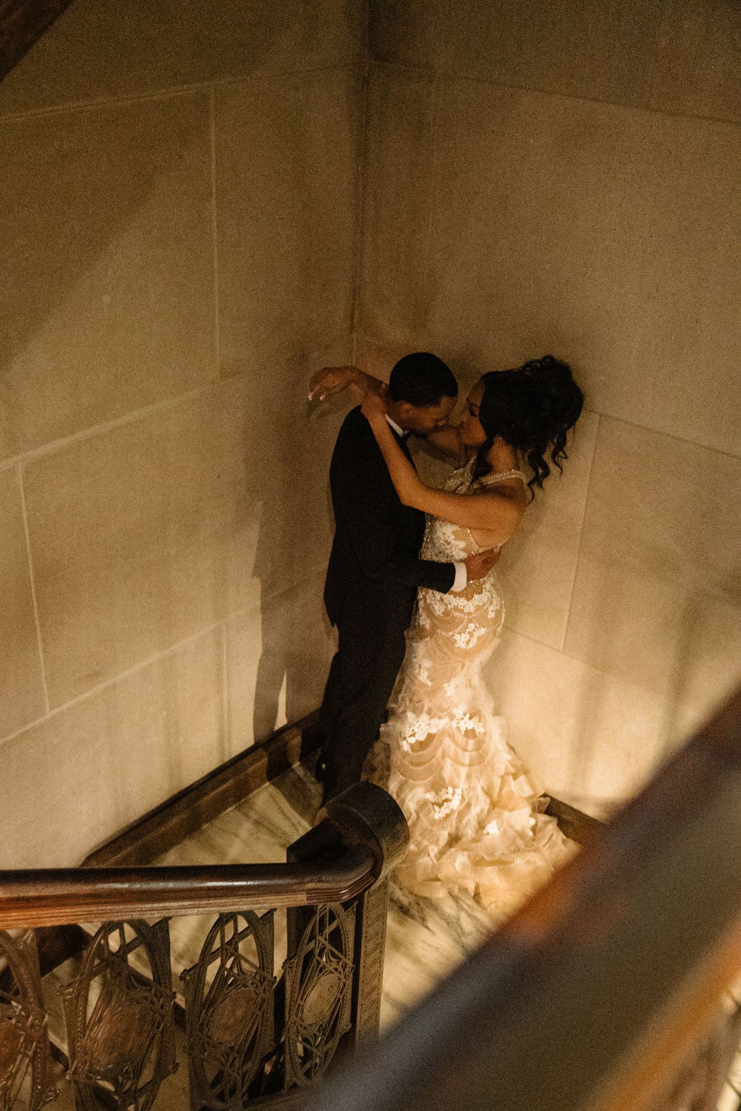 A person in dark clothing climbs up a dimly lit staircase while holding onto the railing.