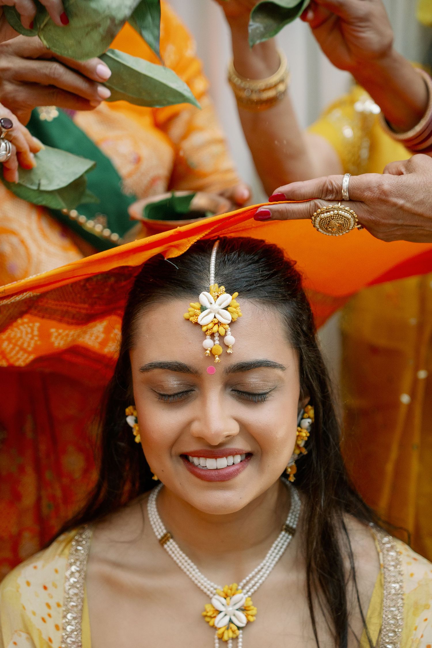 Smiling Indian bride in yellow lehenga with maang tikka during traditional Hindu wedding ceremony ritual.