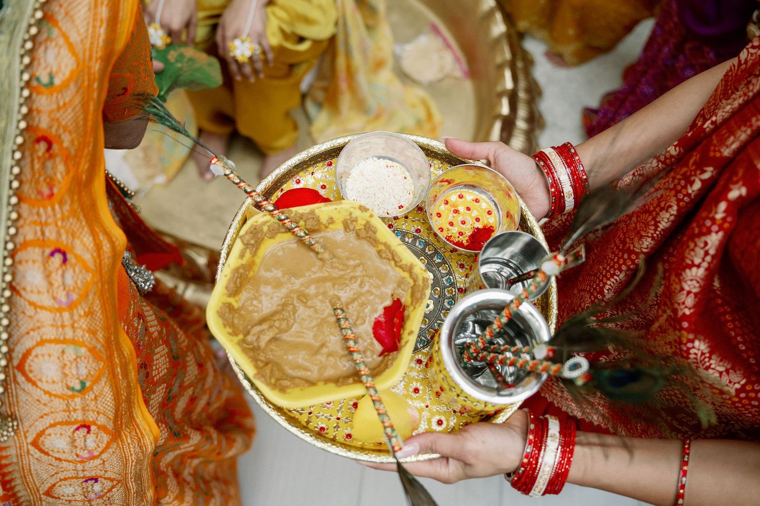 Hands holding a traditional Hindu puja thali with offerings, sweets, and ceremonial items during a religious ritual.