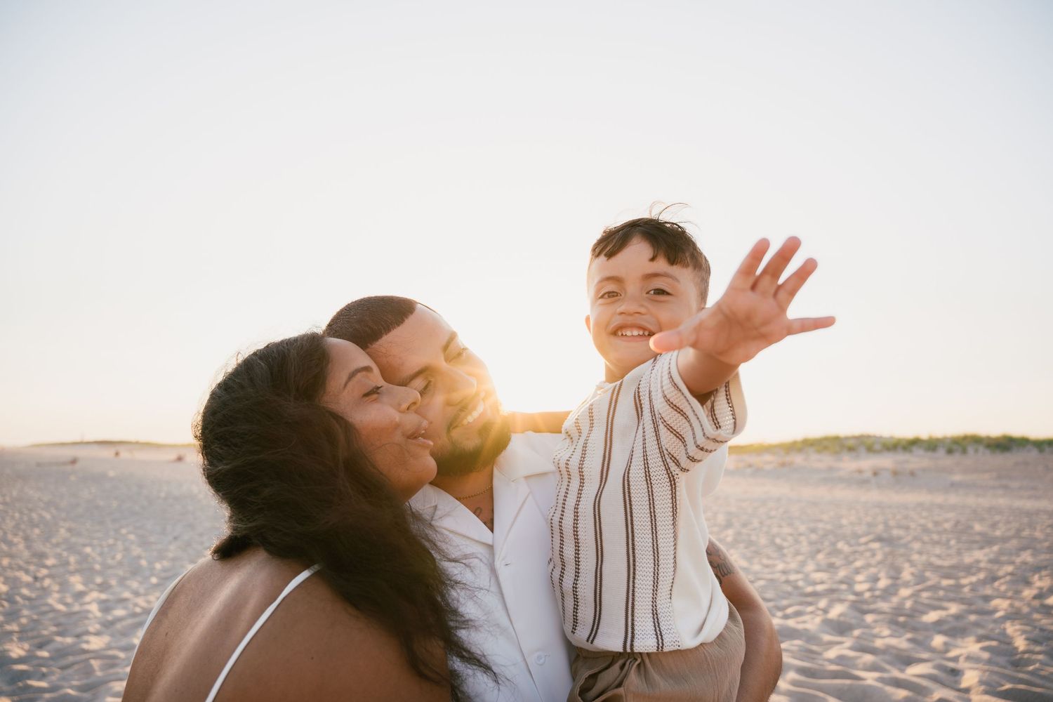 A joyful family moment captured at sunset on the beach with arms raised in celebration.