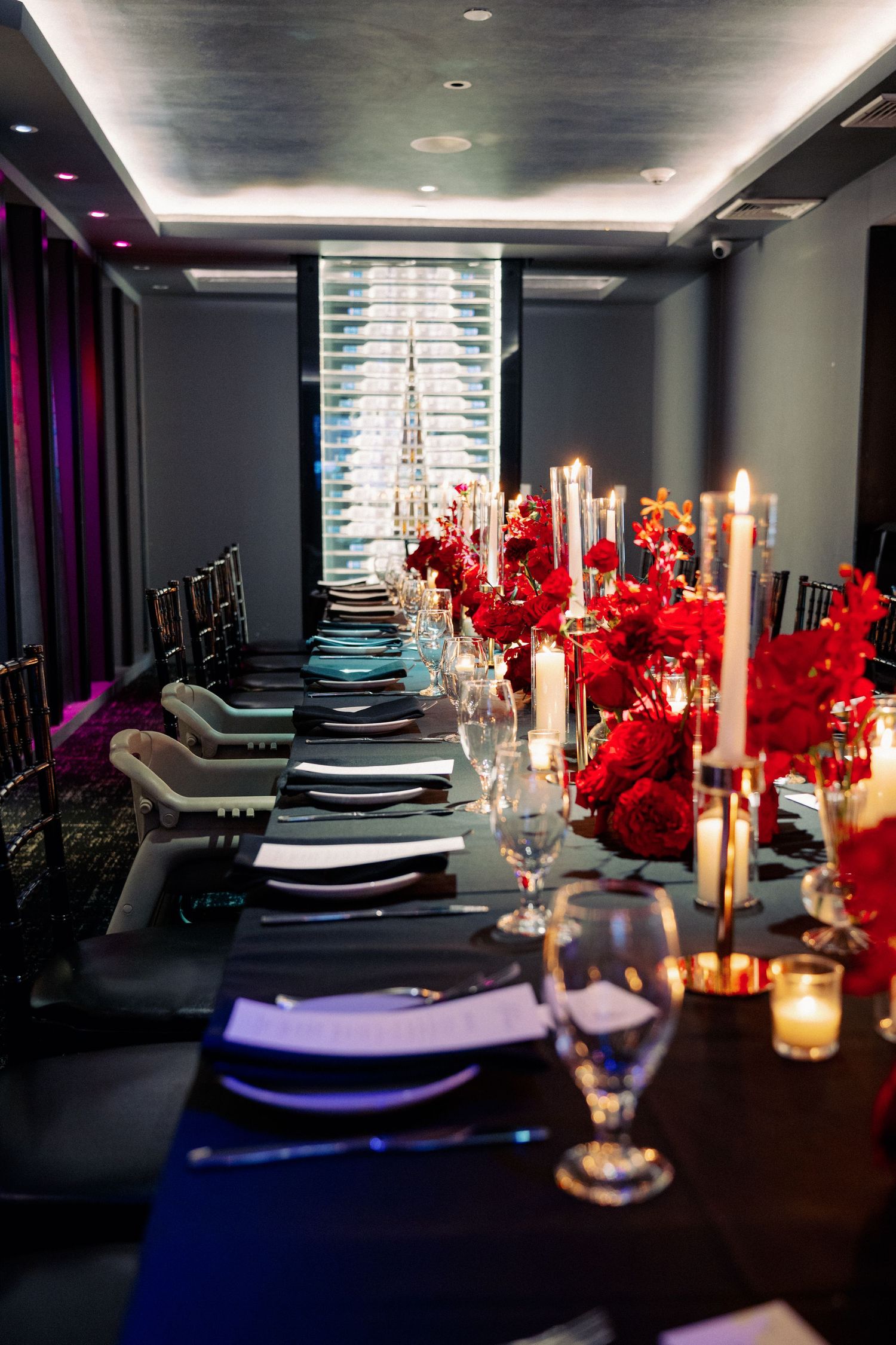 Elegant banquet table with red rose centerpieces, tall candles, black linens, and crystal glassware in a dimly lit dining room.