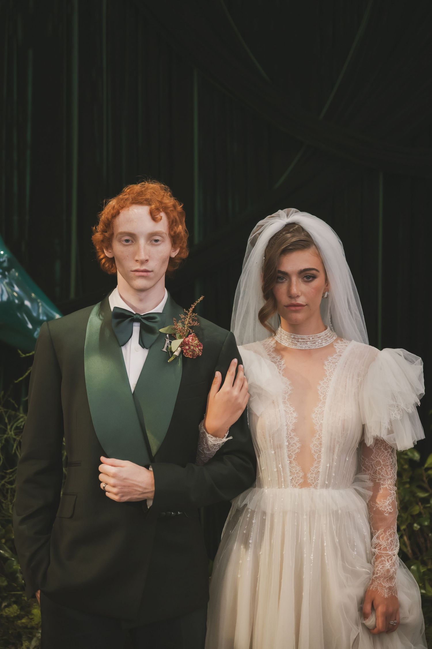 A couple in vintage-inspired wedding attire with a dark green suit and lace dress pose together for portraits.