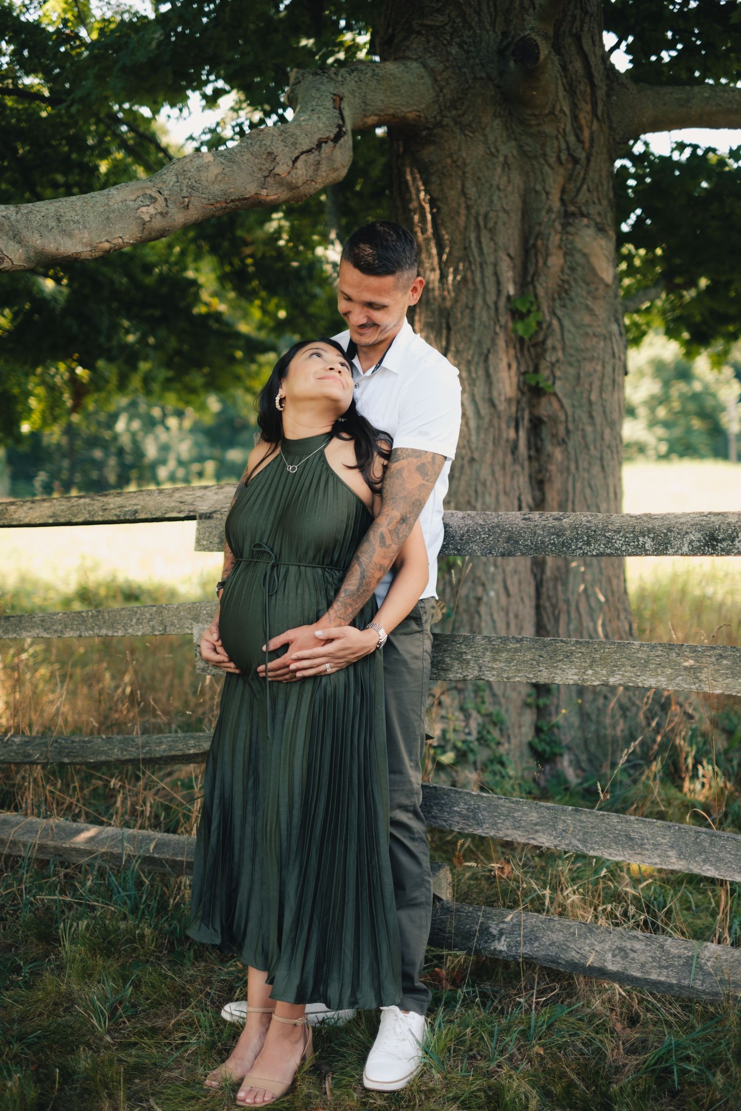 Romantic maternity photoshoot by a rustic wooden fence in golden evening light.