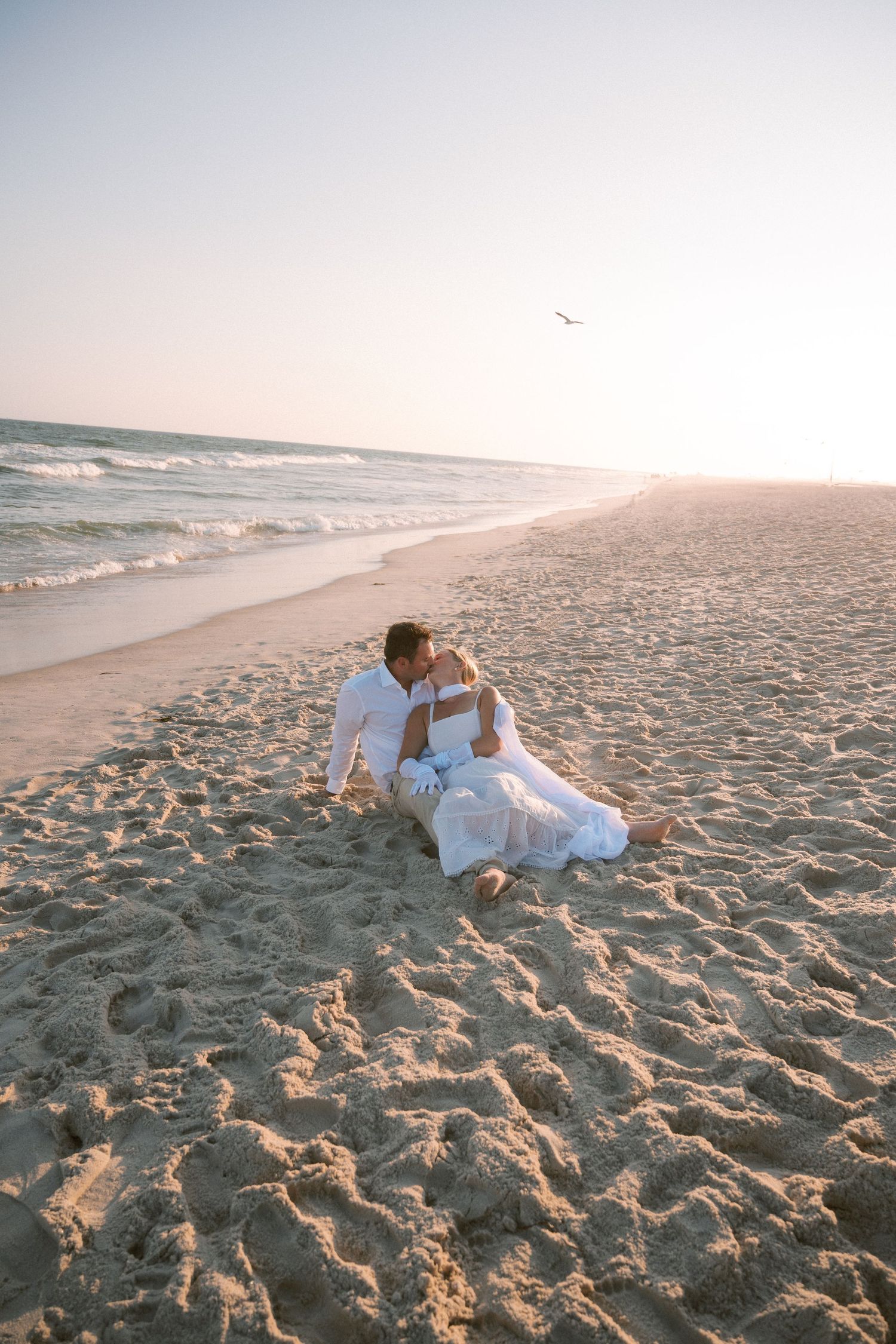 A couple relaxes together on a sandy beach during golden hour.