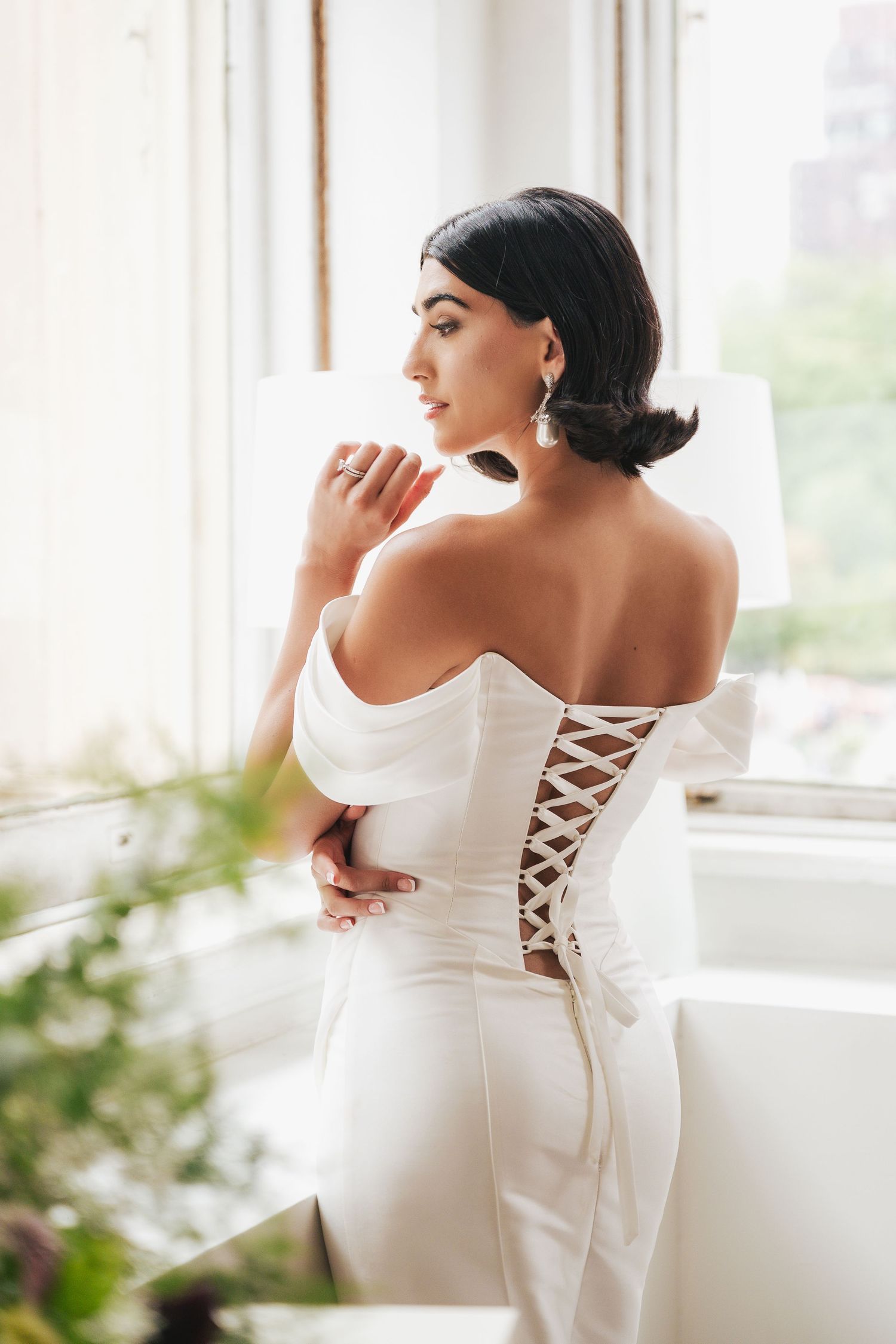 Back detail of white bridal gown showing corset-style lacing in natural window light.