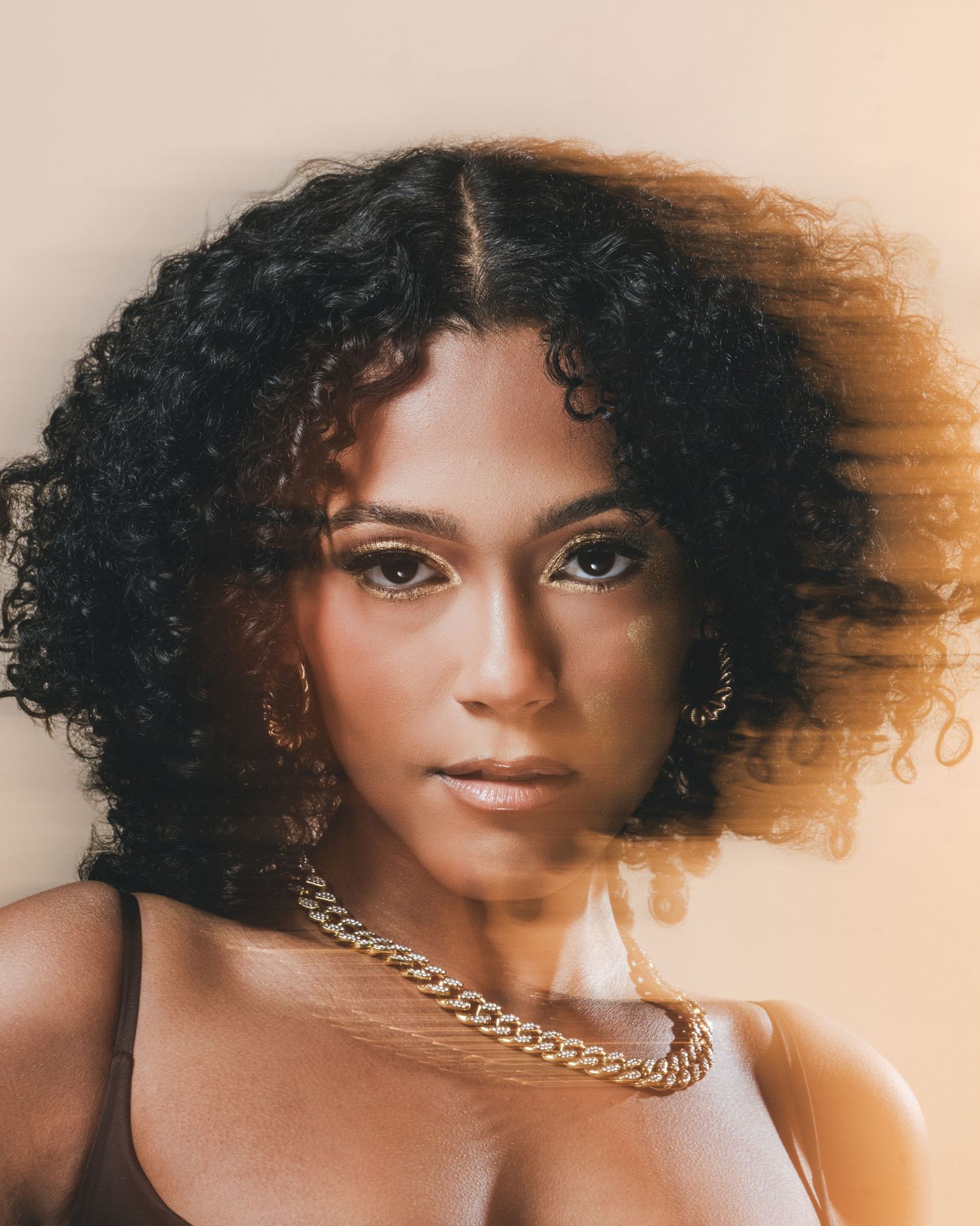 A series of portrait shots showing a woman with curly natural hair and gold chain necklace against a warm-toned background.