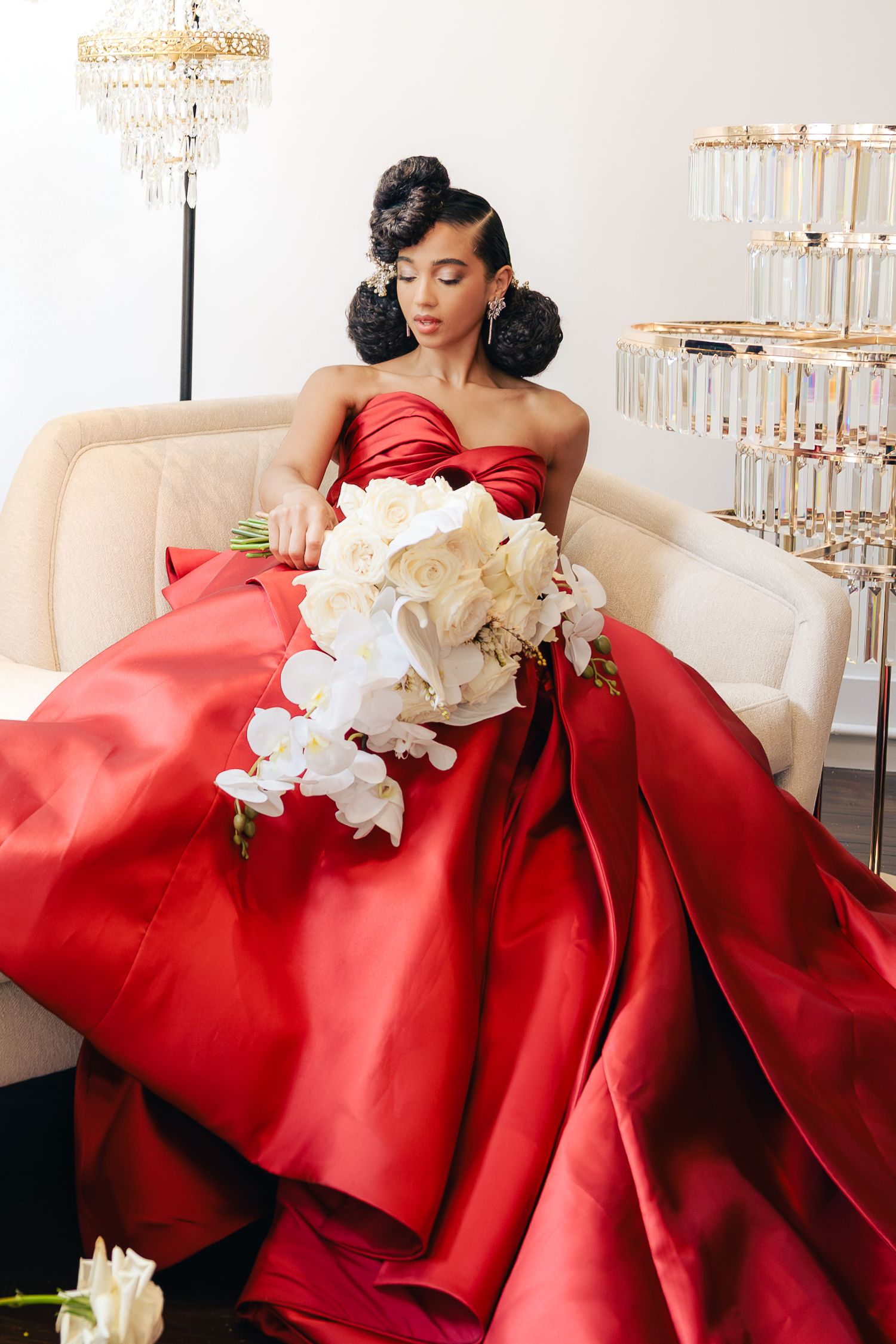 Glamorous portrait in a red satin ball gown with white orchids on cream furniture.
