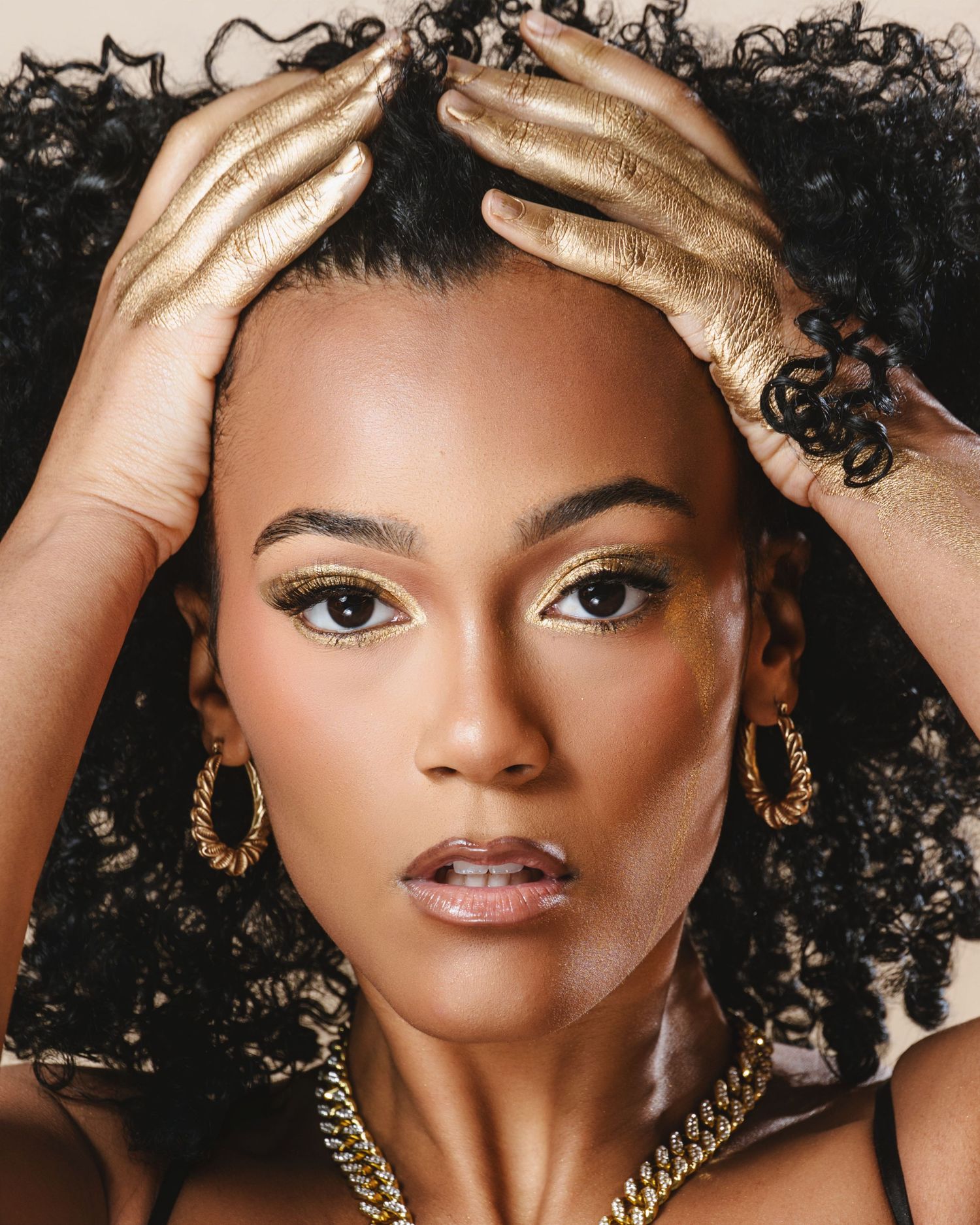 Close up beauty portrait showing natural curly hair and gold jewelry against dark textured background.