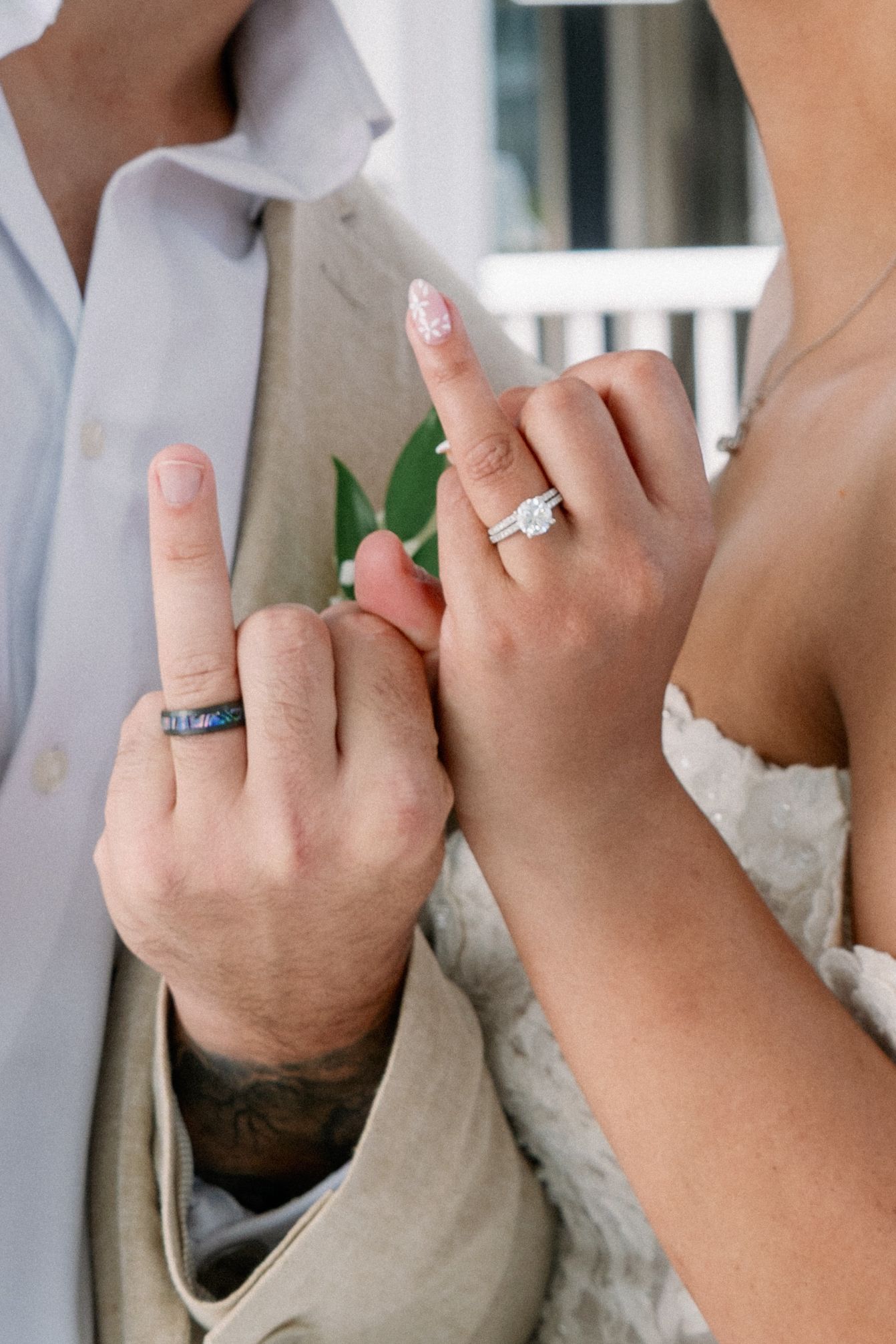 Newlywed couple showing off their wedding rings, her diamond engagement ring and his colorful band, in a lace gown and linen suit.