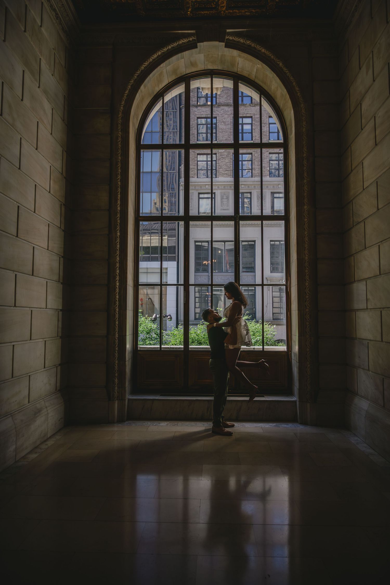 Silhouettes stand in a stone building with dramatic arched windows letting in natural light.