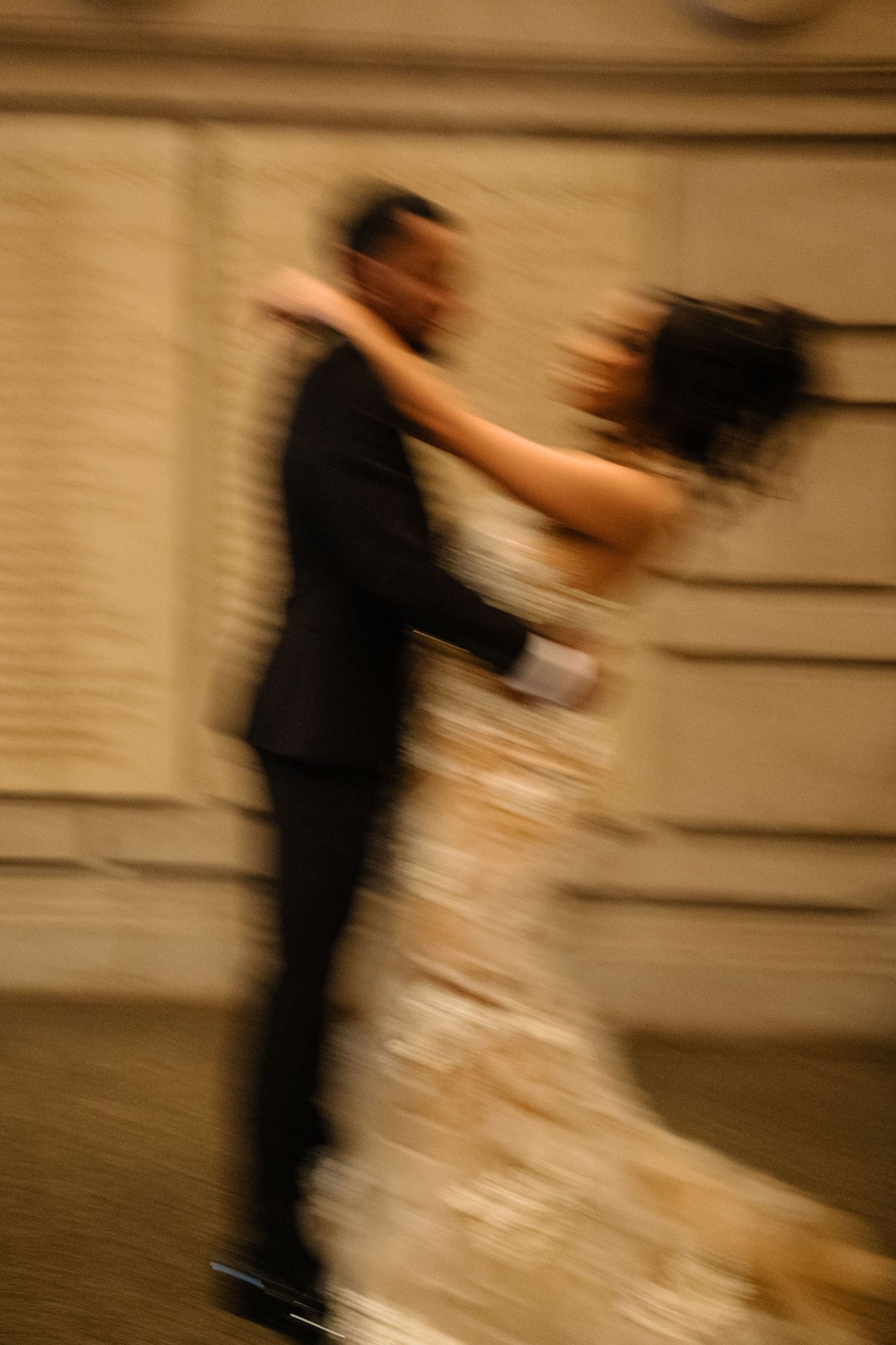 A blurred motion shot of a couple dancing at a formal event, with the woman wearing a white dress and man in black suit.