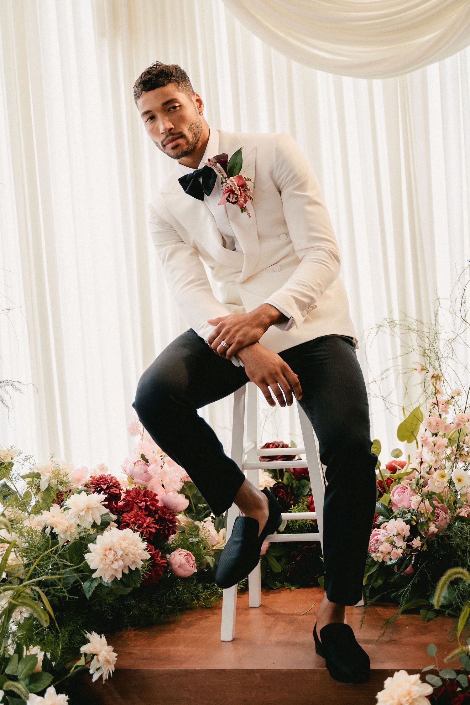 Modern groomsmen in white shirts and dark pants posed casually among pink and red flowers.