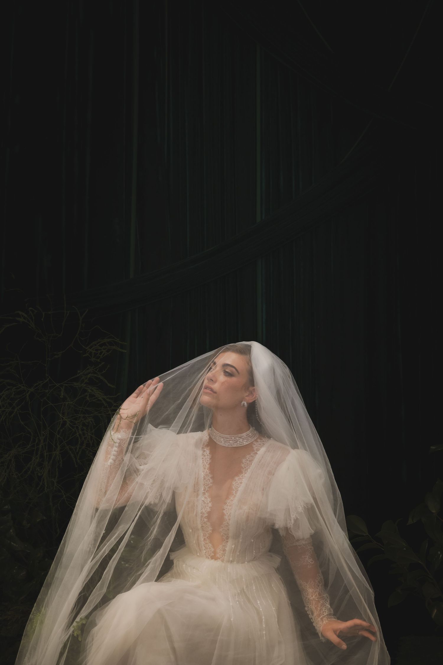 Ethereal bridal portrait featuring a flowing white veil and lace wedding gown against a dark background.