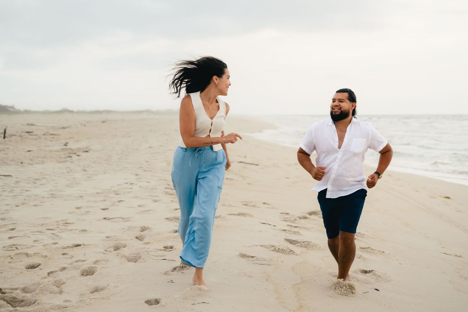 A playful couple runs and chases each other along the beach shore.