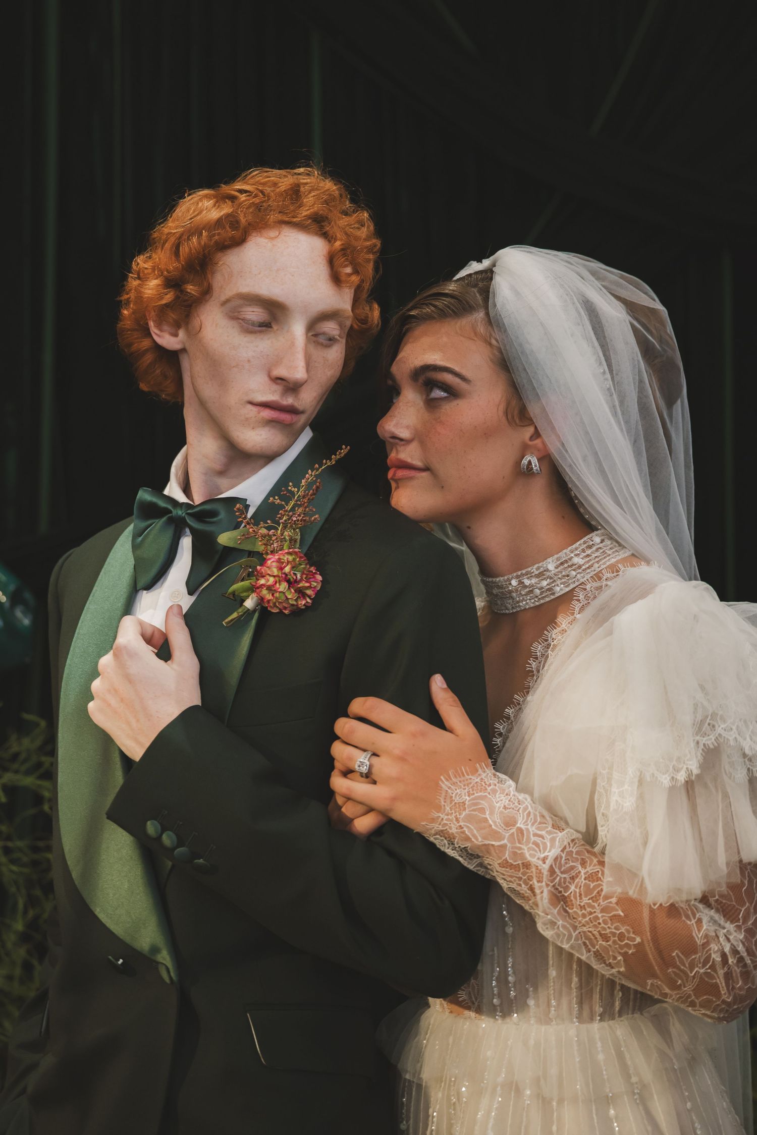 A romantic wedding portrait featuring a couple in vintage-inspired attire with a green suit and lace veil.