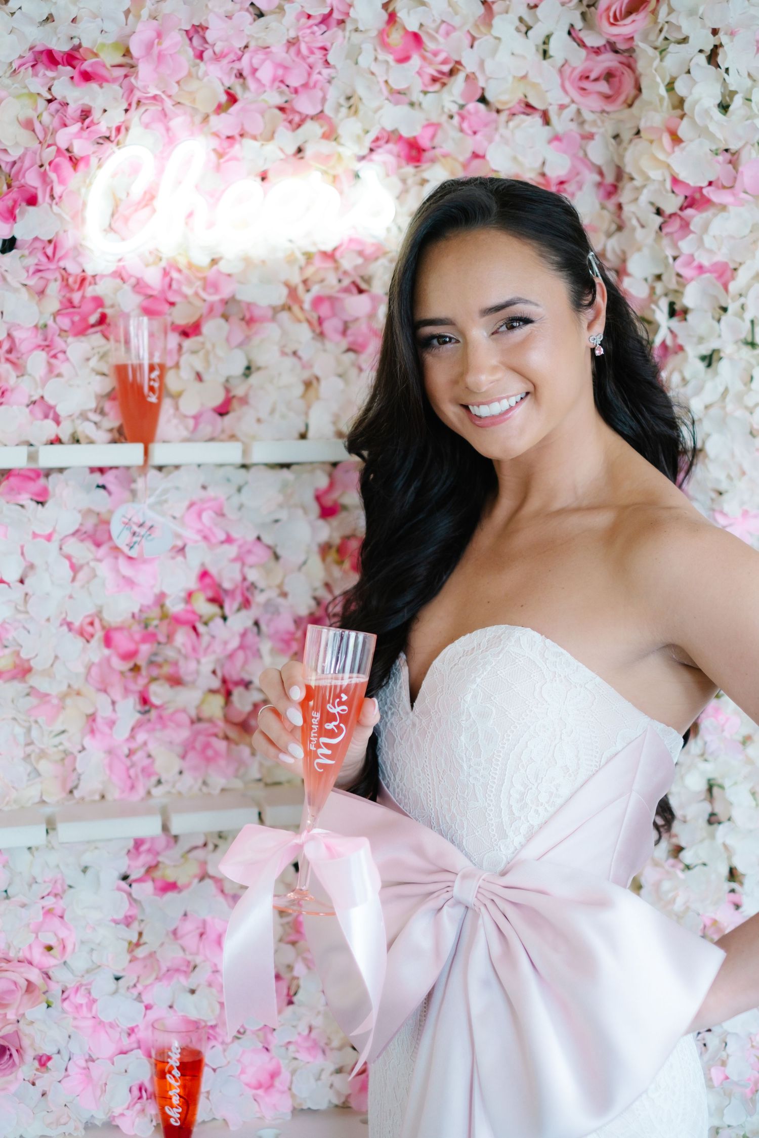 Elegant white dress with pink bow against floral wall backdrop.