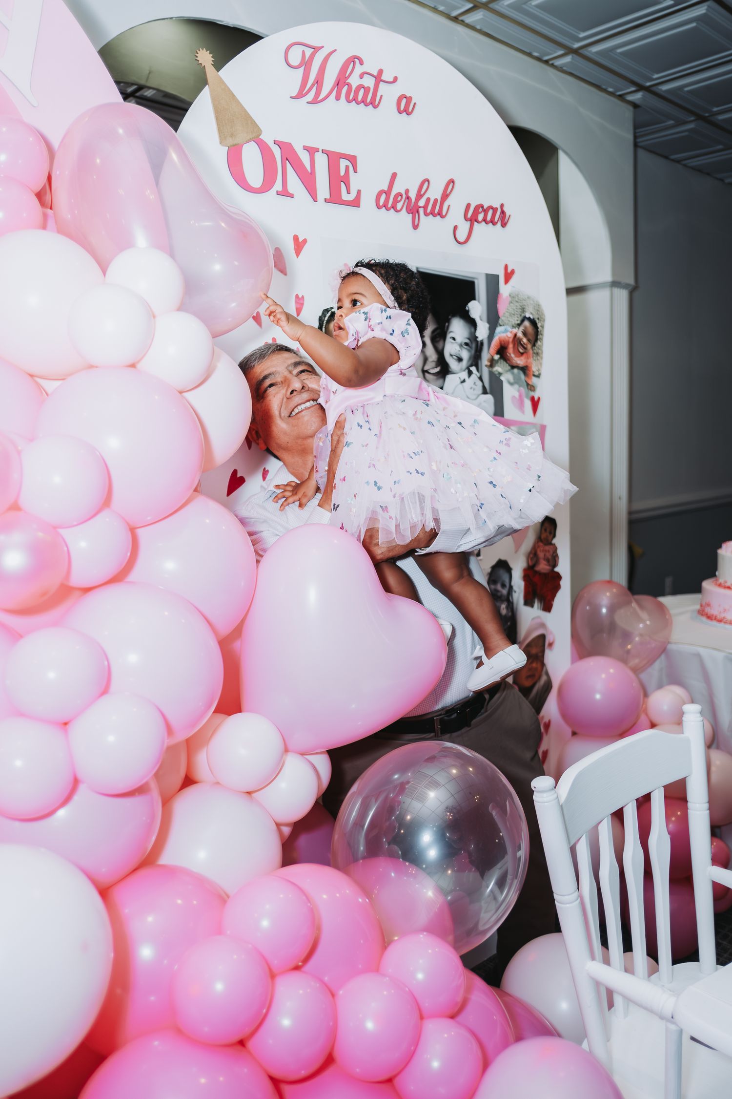 Pink and white balloons create a festive backdrop for a first birthday celebration with party decorations.
