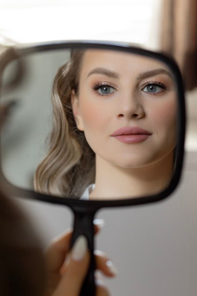 Bride checking her reflection after bridal makeup by Natalia MUA, elegant soft glam look in Winnipeg.