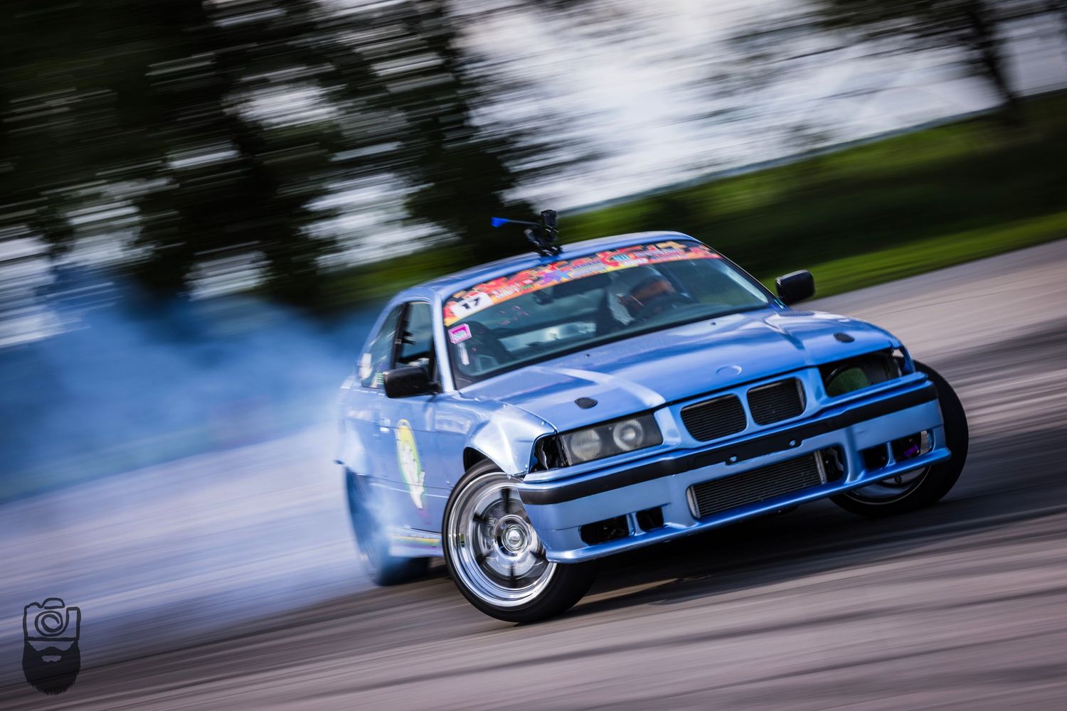 Blue BMW drift car sliding sideways with smoke trails.