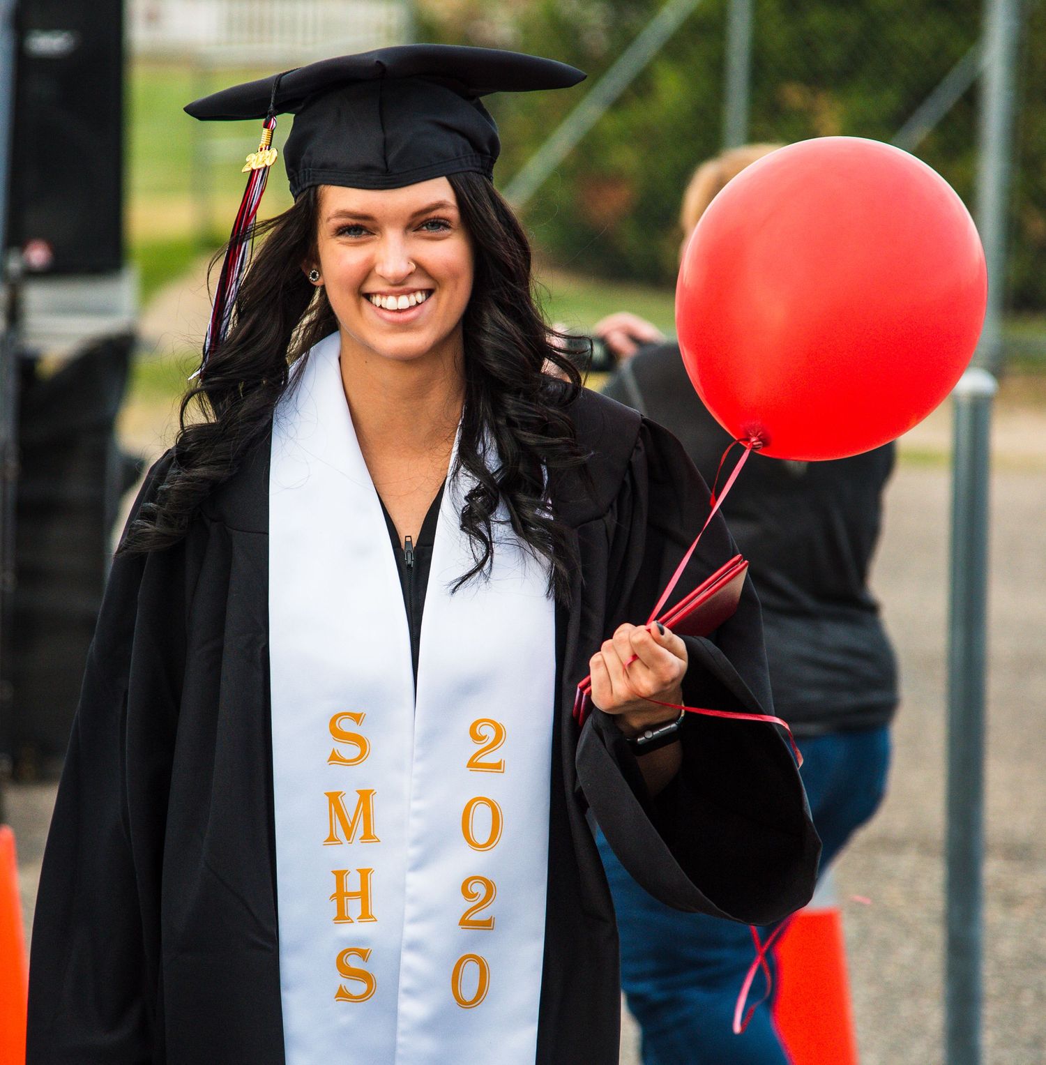 Graduate in black cap and gown holding red balloon during celebration.
