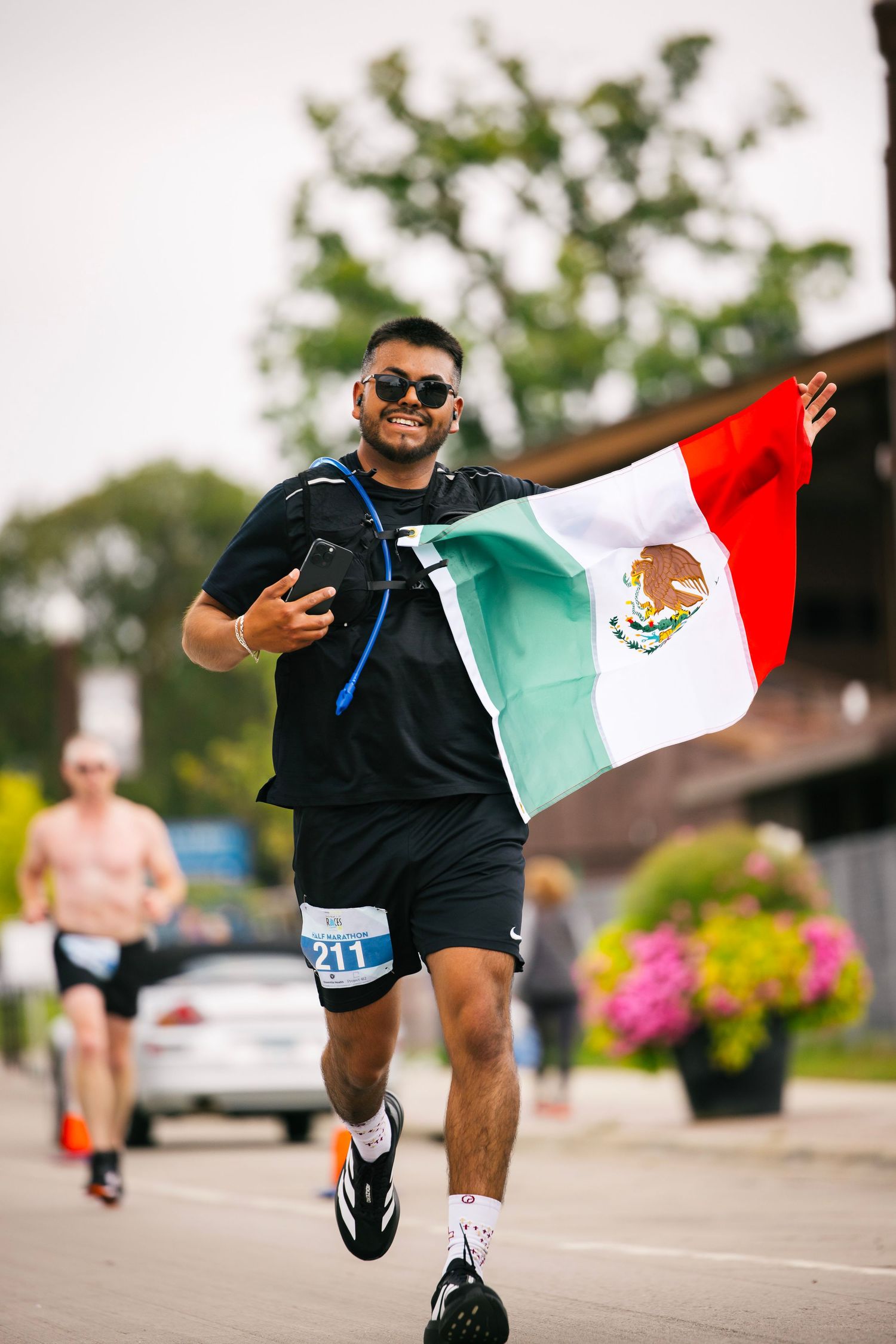 Runner carrying Mexican flag sprints energetically during outdoor race event.