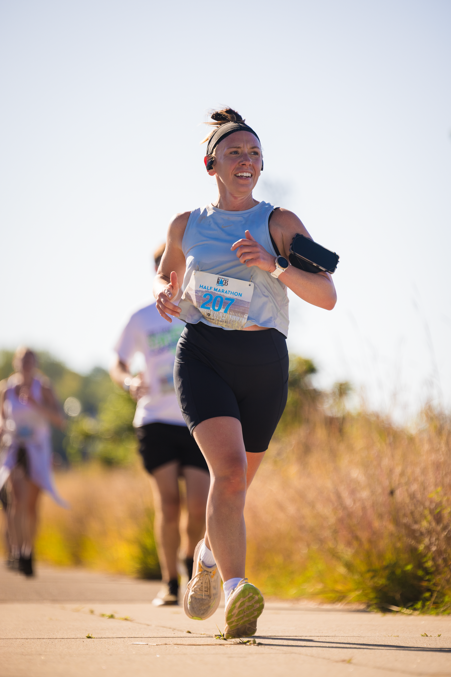 Runner with race bib strides energetically along a sunny trail during an outdoor competition.