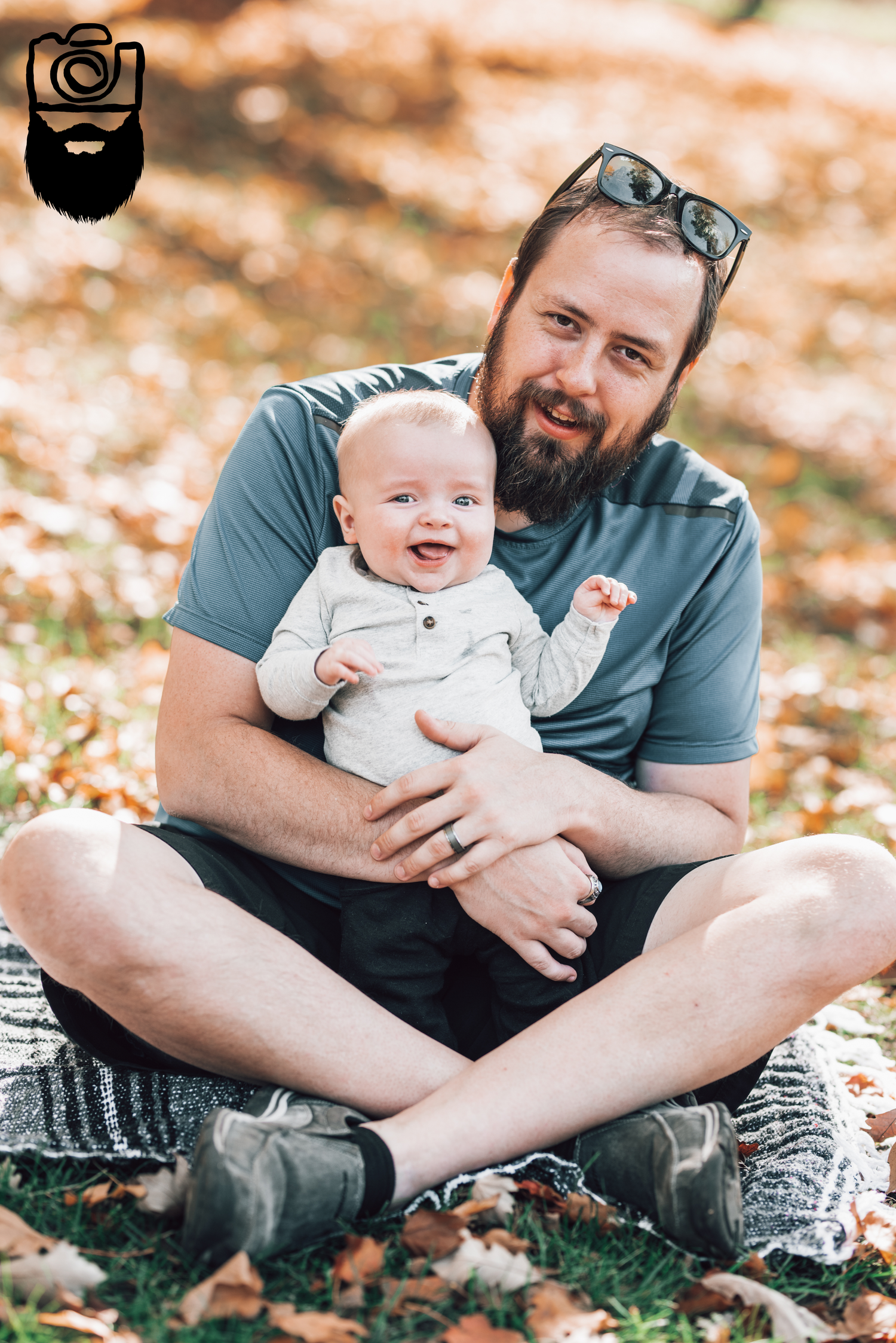 Parent sitting cross-legged on blanket holding smiling baby outdoors.