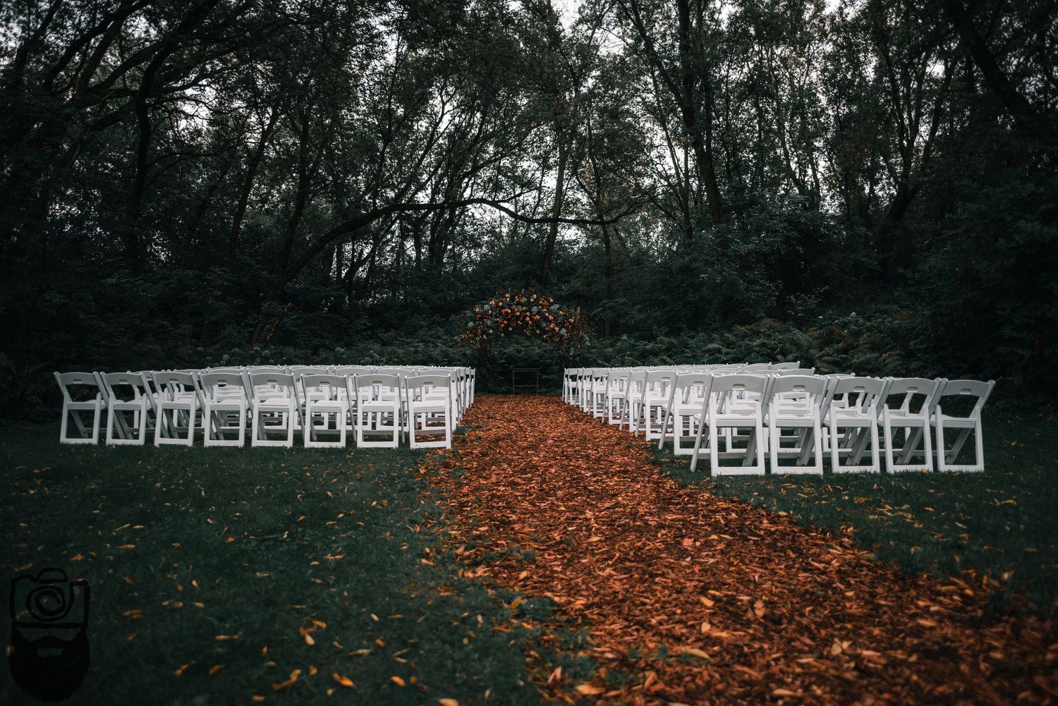 Outdoor wedding ceremony setup with white chairs arranged in rows on fallen autumn leaves.